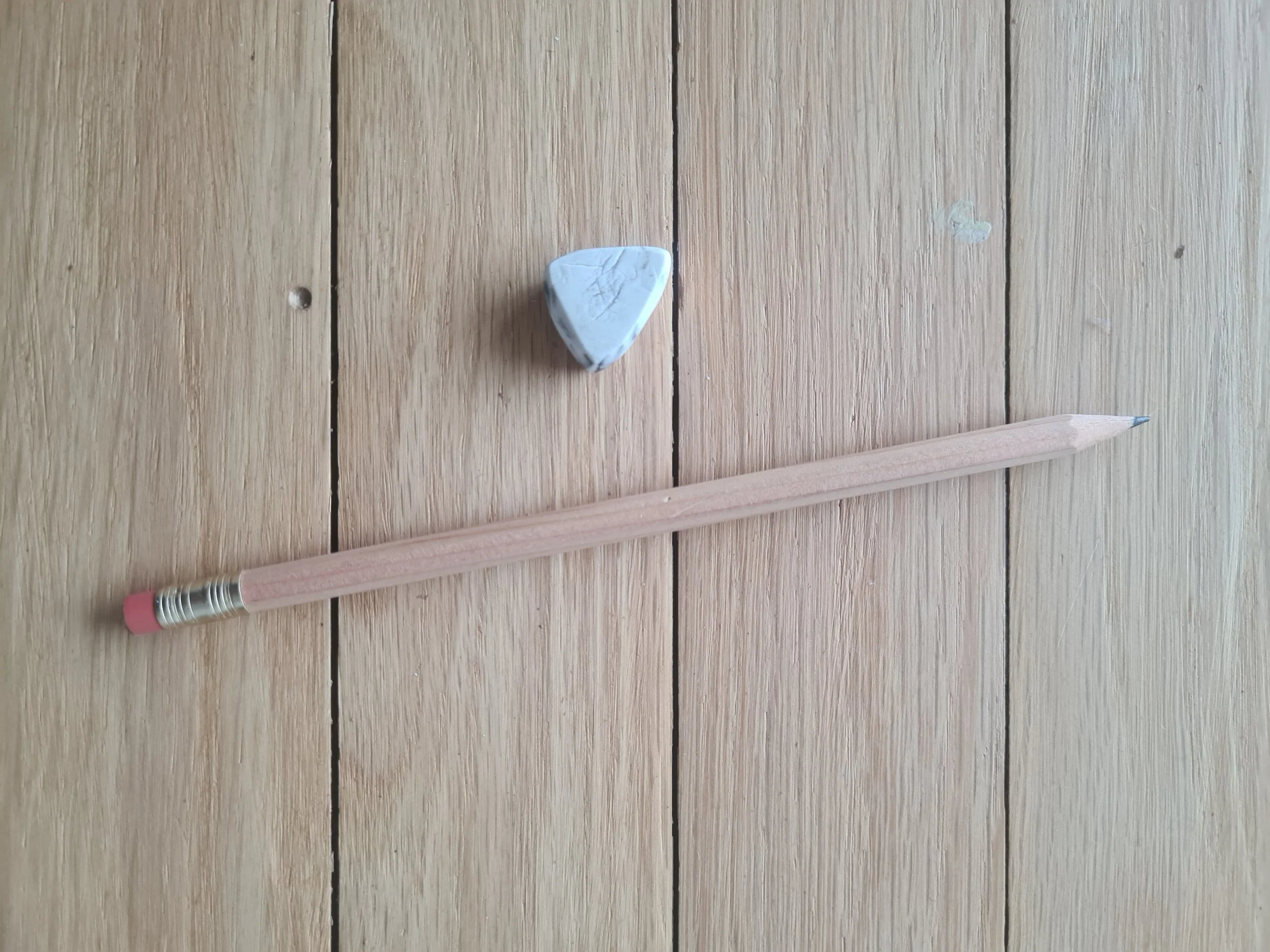 A wooden pencil with a pink eraser and metal band, a white eraser, and a wooden surface with visible grain and cracks.