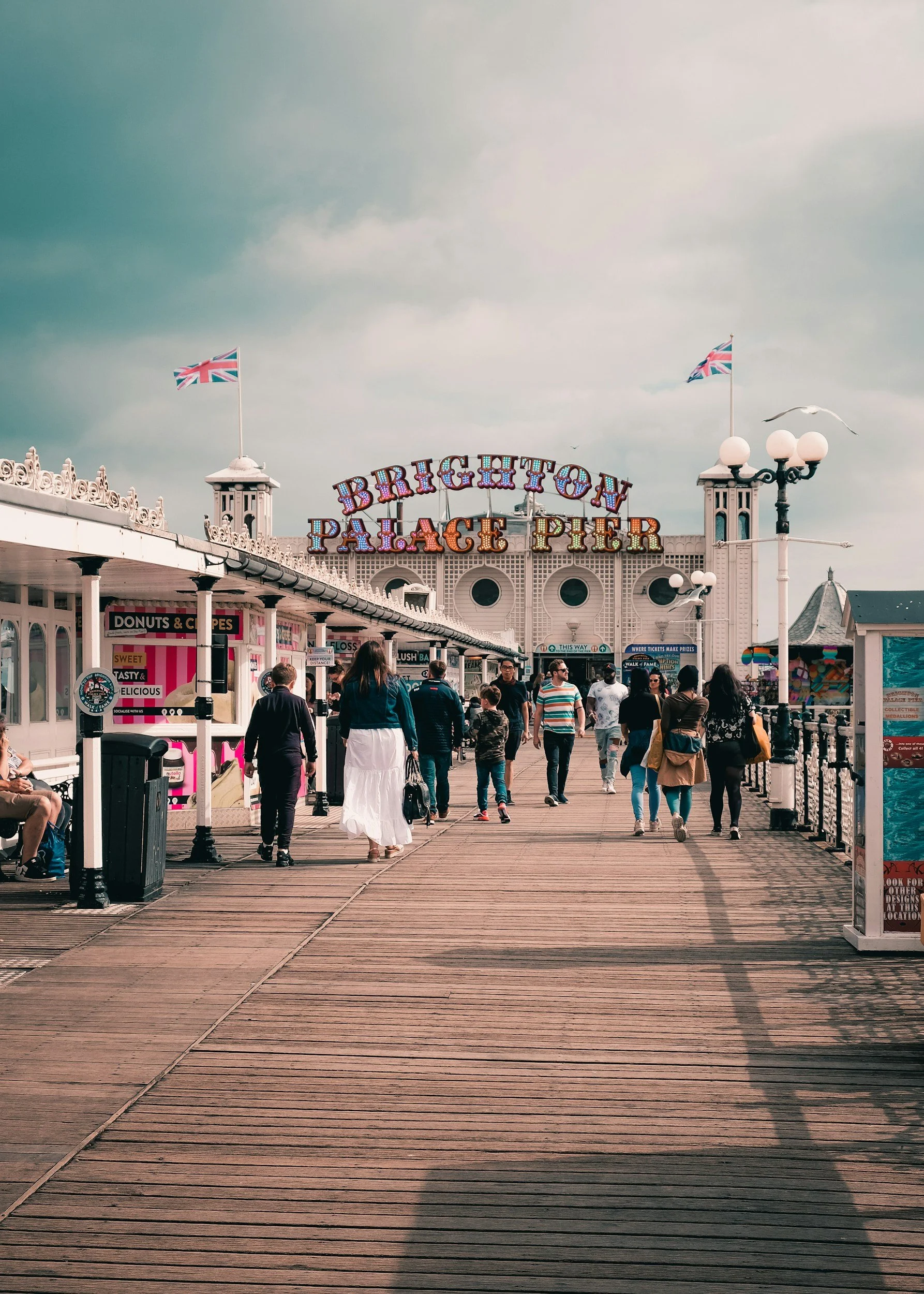 People walking on a pier at Brighton Palace Pier with the sign and Union Jack flags in the background.