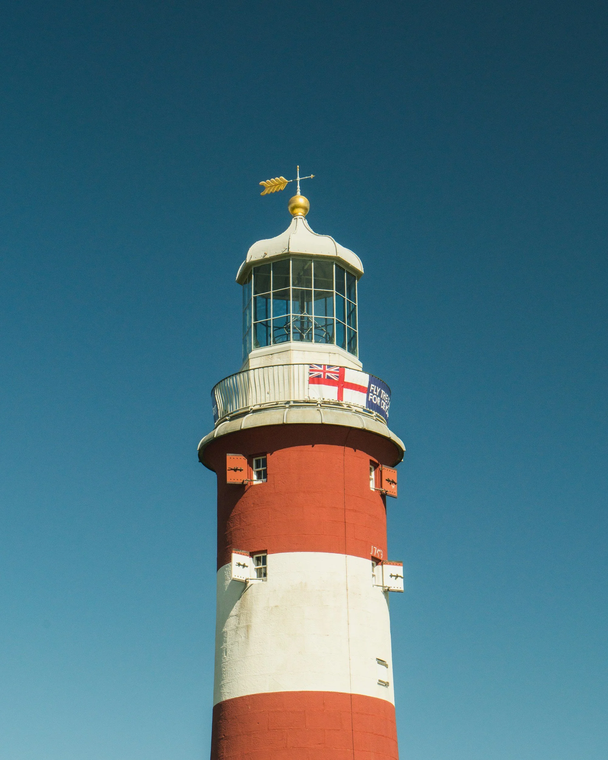 A lighthouse with red and white horizontal stripes under a clear blue sky.