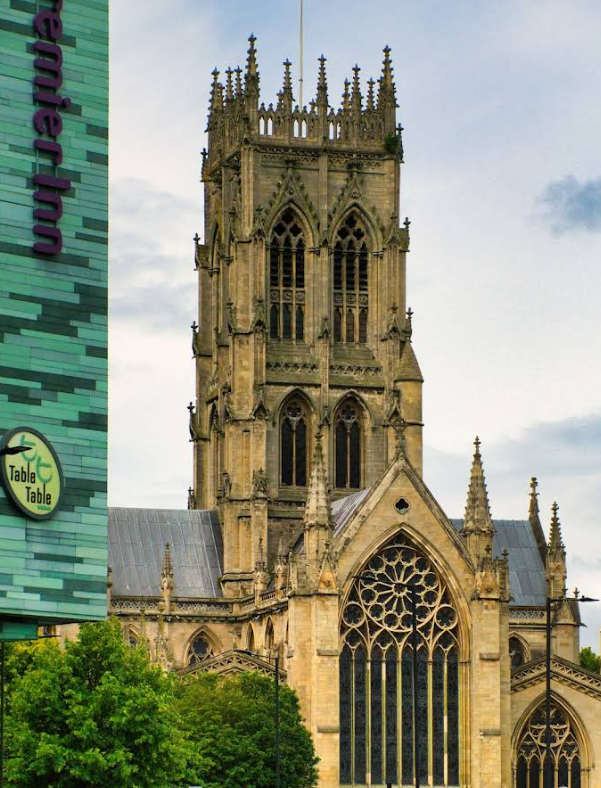 A view of a Gothic-style cathedral with tall spires and large stained glass windows, situated next to a modern building with a green facade.