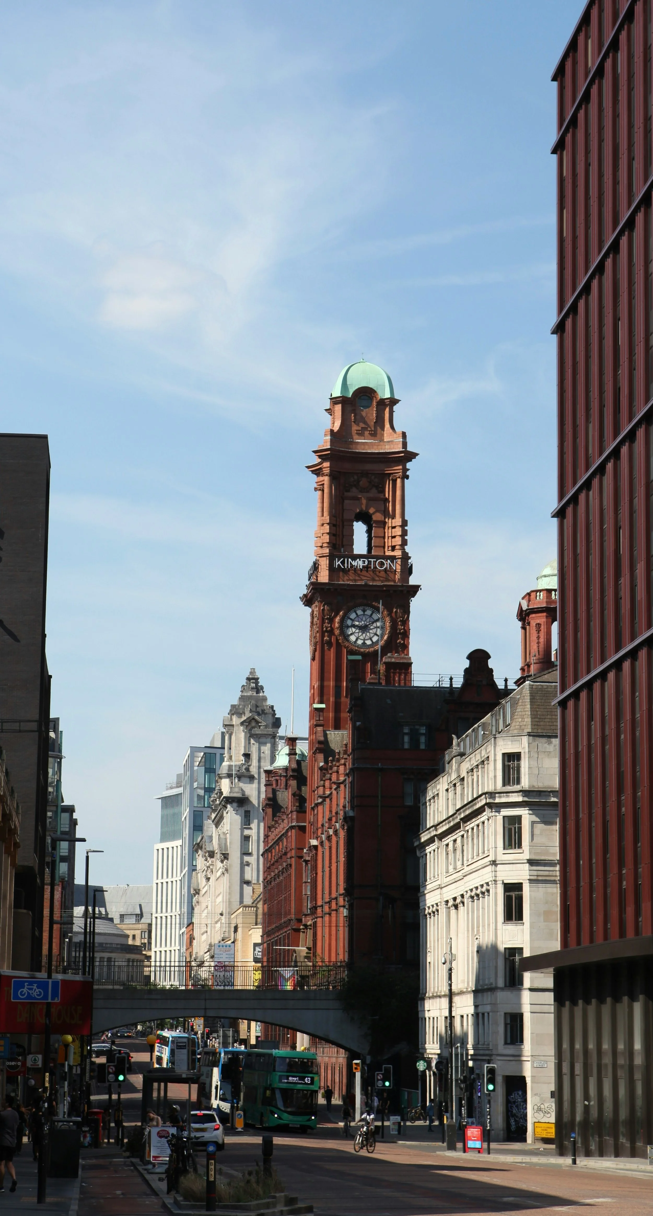 Street scene in daytime with historic clock tower labeled 'KIMPTON' in central London, surrounded by modern and historic buildings, cars, buses, and pedestrians.