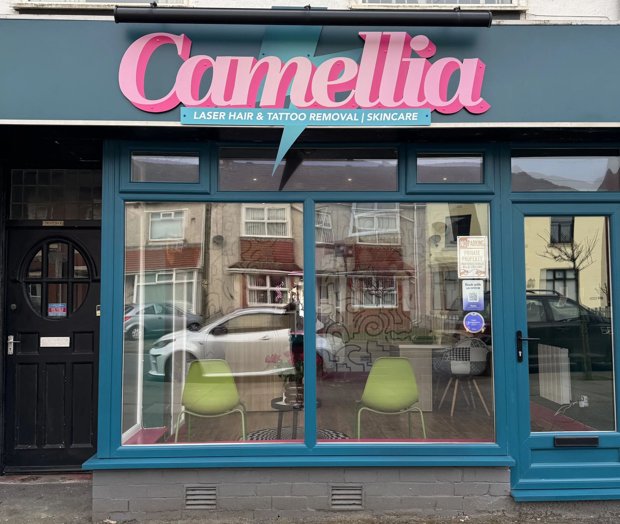 storefront for 'Carmella' with pink sign, offering laser hair and tattoo removal and skincare, with large windows showing interior seating and reflections of street and parked cars.