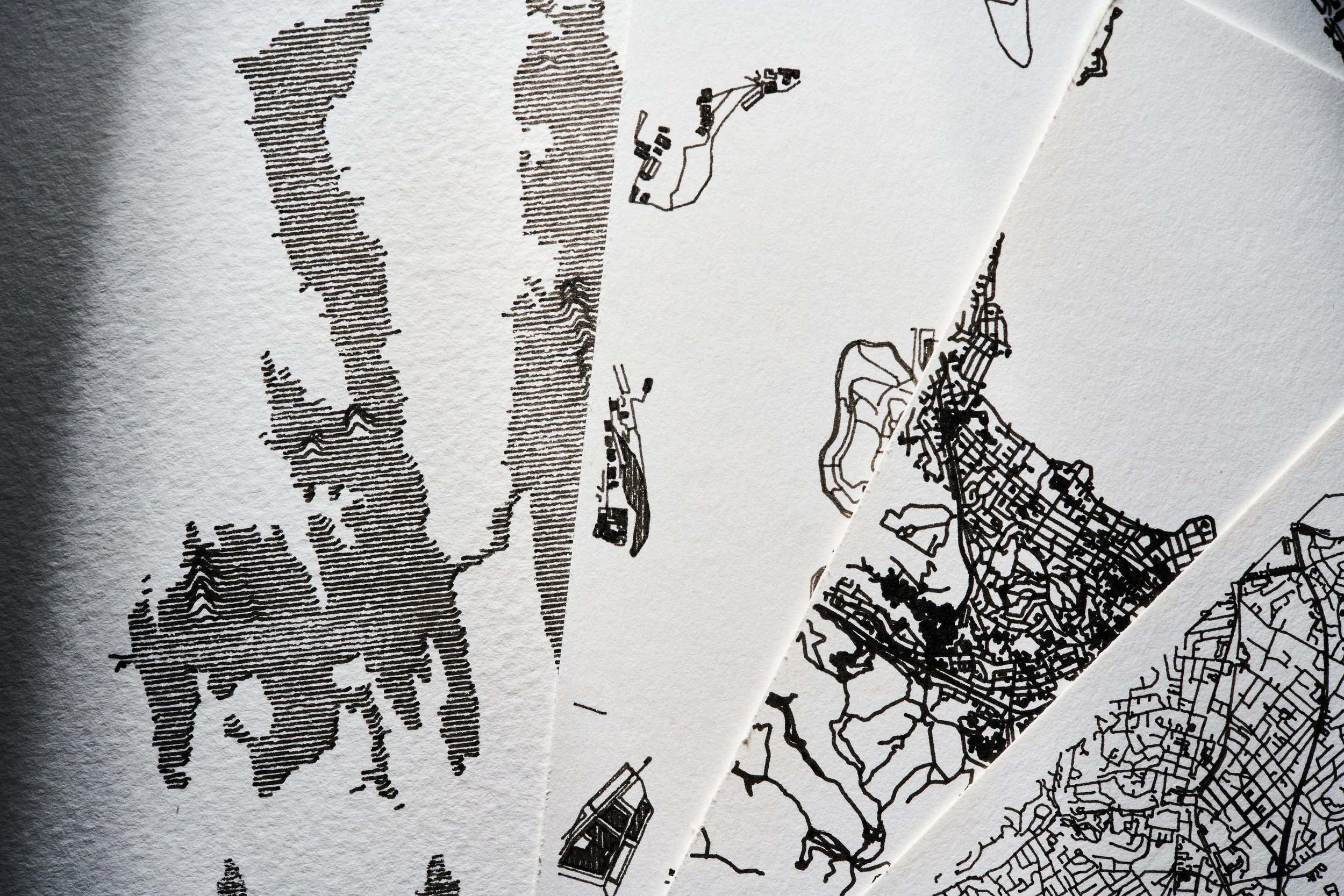 Close-up of black line drawings on white paper, depicting maps and landscapes with various land features and structures.