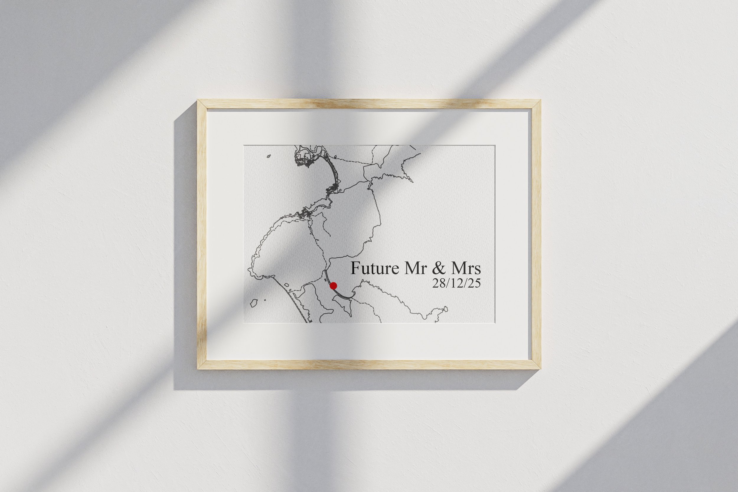 A framed wedding announcement with a minimalist map, a red dot marking a location, and text reading "Future Mr & Mrs, 28/12/25," on a white wall with shadows.