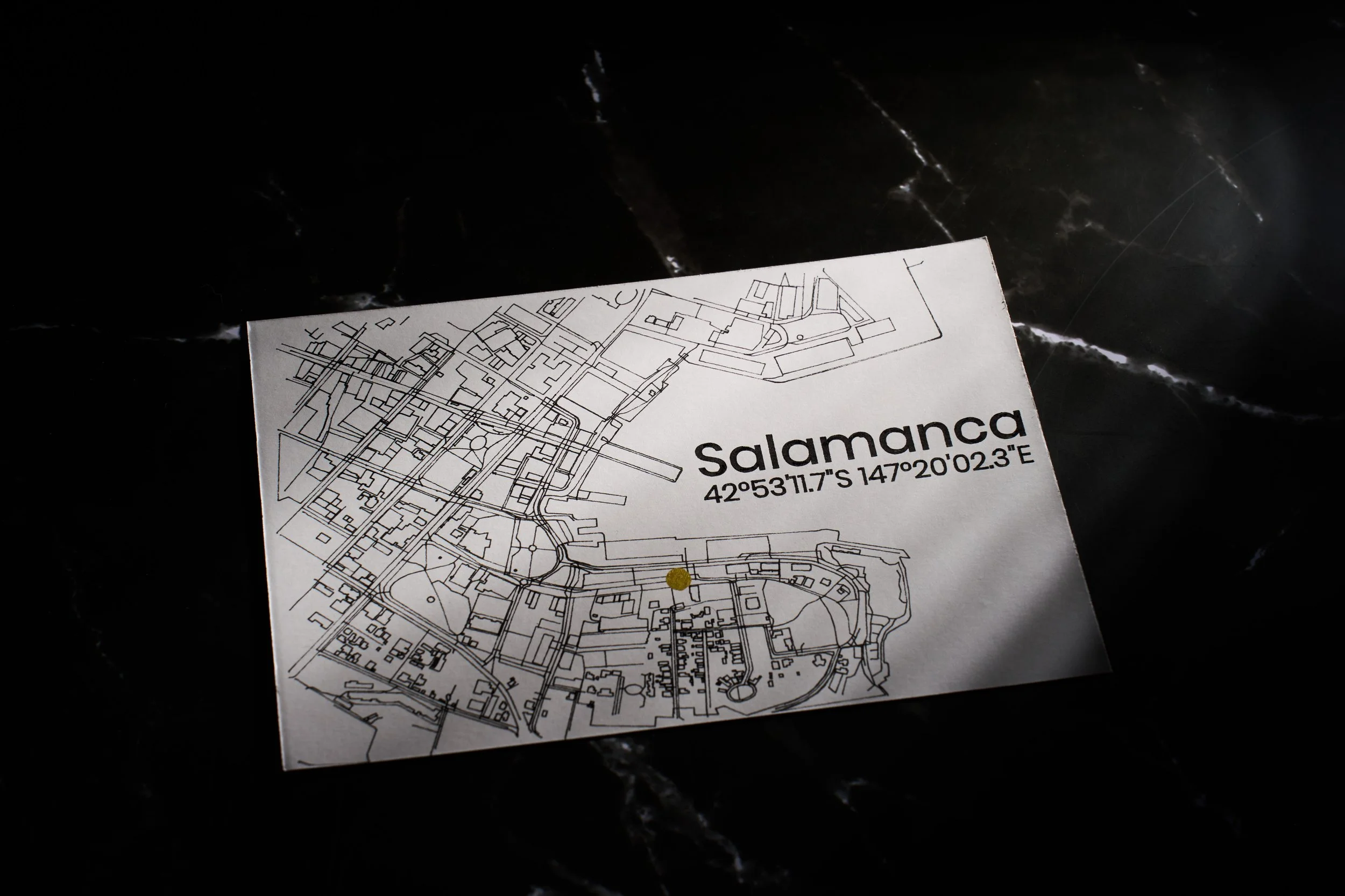 A black and white map of Salamanca on a piece of paper with GPS coordinates 42°53'11.7"S 147°20'02.3"E, laid on a dark, Marble surface.