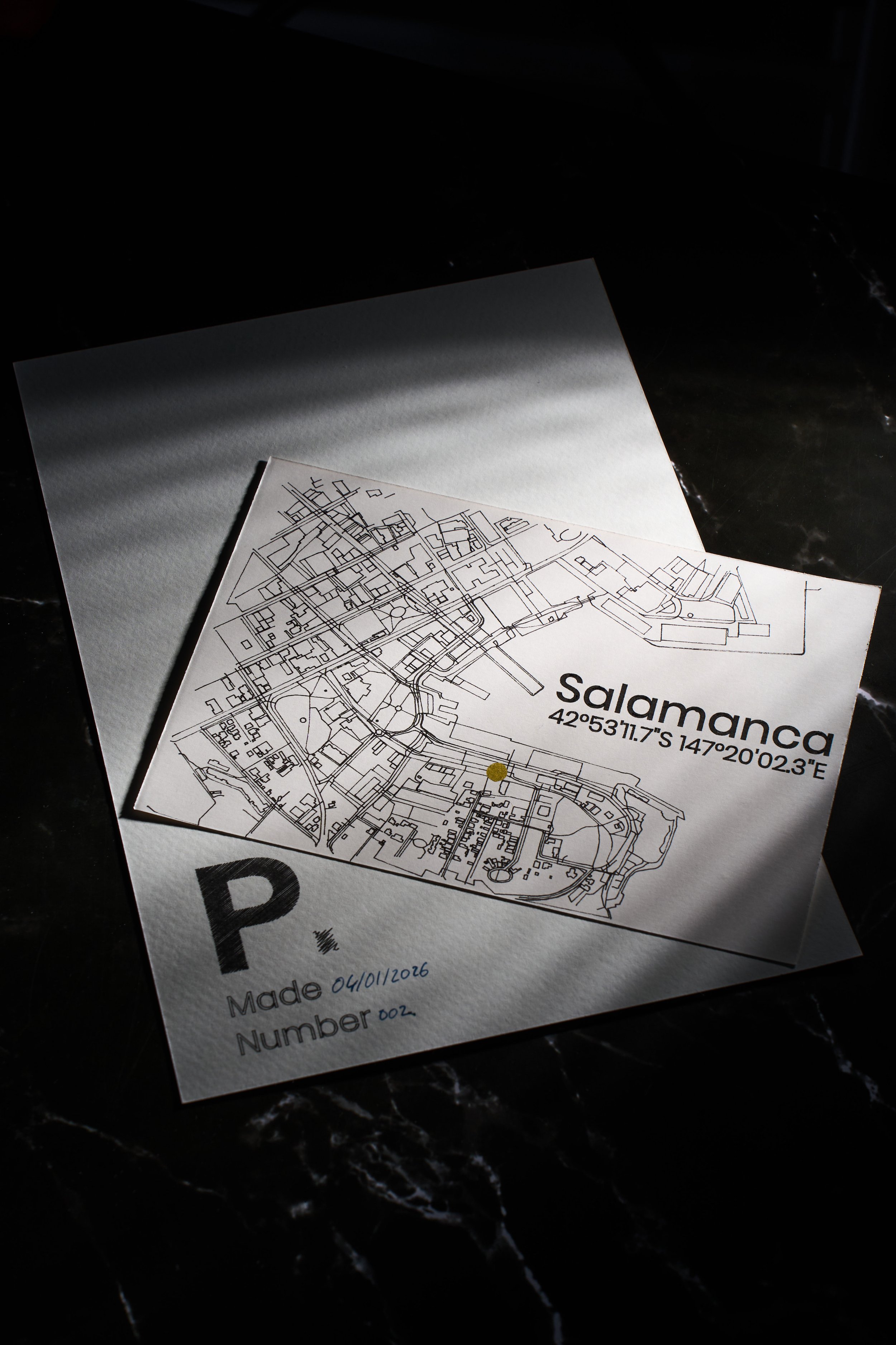 A black and white map of Salamanca with coordinates 42°53'11.7"S 147°20'02.3"E, on top of a white paper with the Plot It P logo symbol, handwritten date 04/01/2016, and number 002, placed on a dark marble surface.