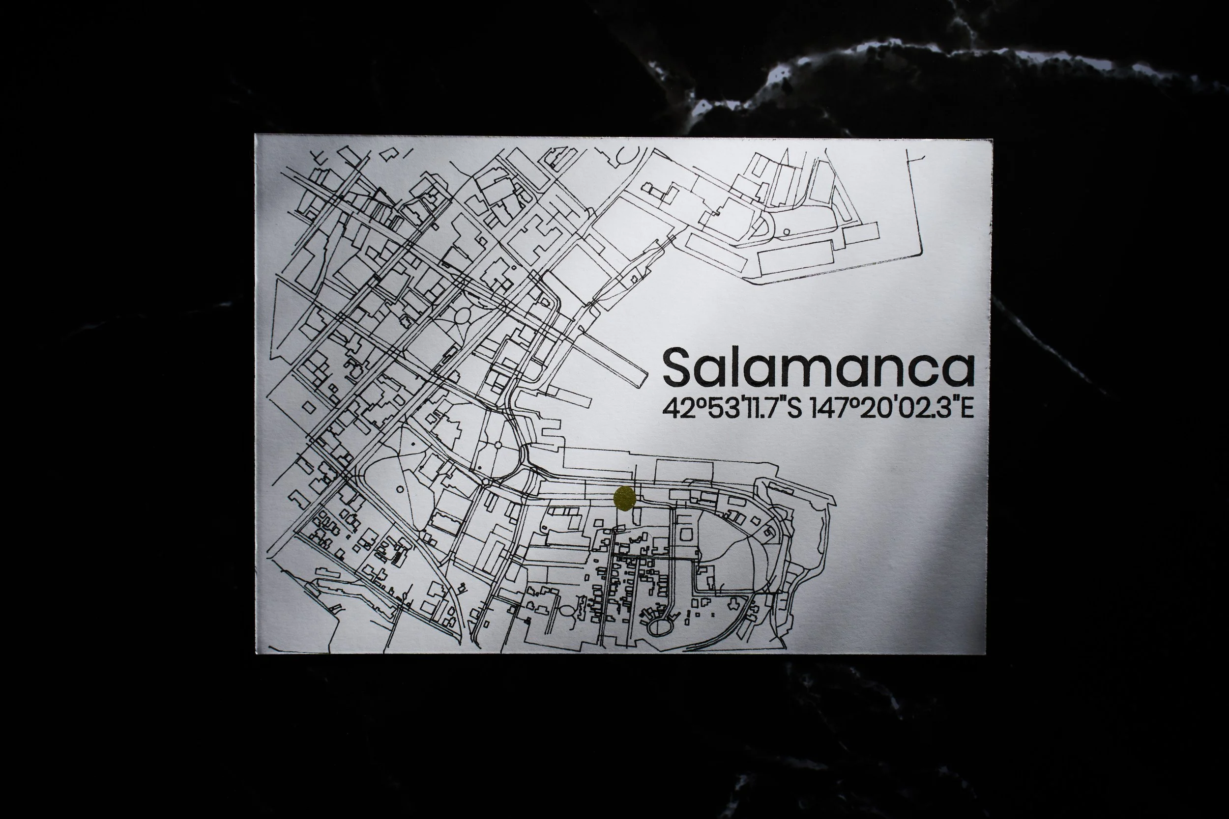A map of Salamanca with the city's name, coordinates, and streets visible in black and white, laid out on a dark surface.