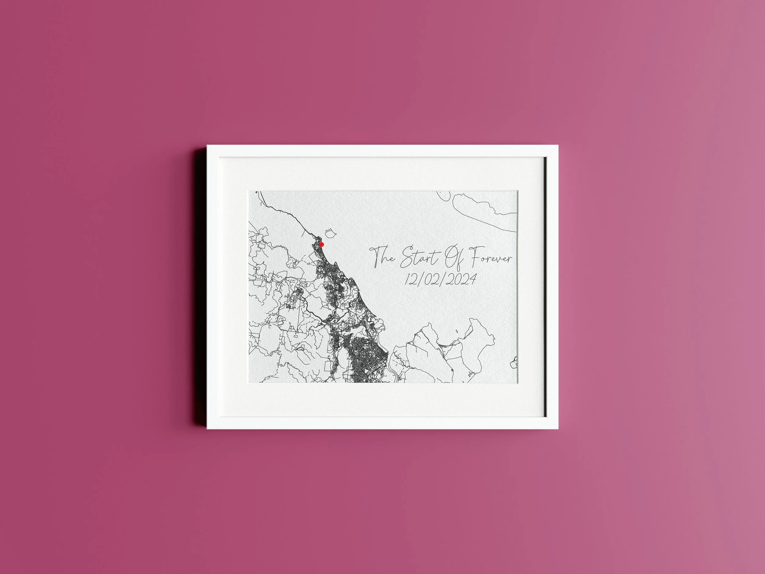 White framed artwork on a pink wall featuring a black and white map with a red dot, handwritten text that says "The Start Of Forever" and the date "12/02/2024".
