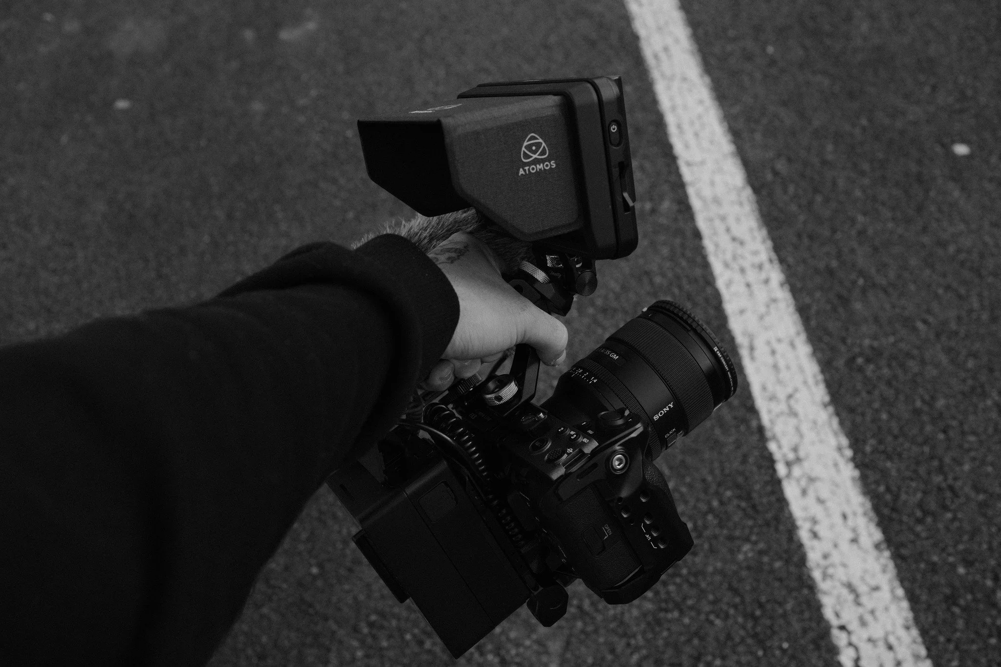Une main tient un appareil photo Sony avec un filtre à objectif, à l'extérieur sur une route avec une ligne blanche.