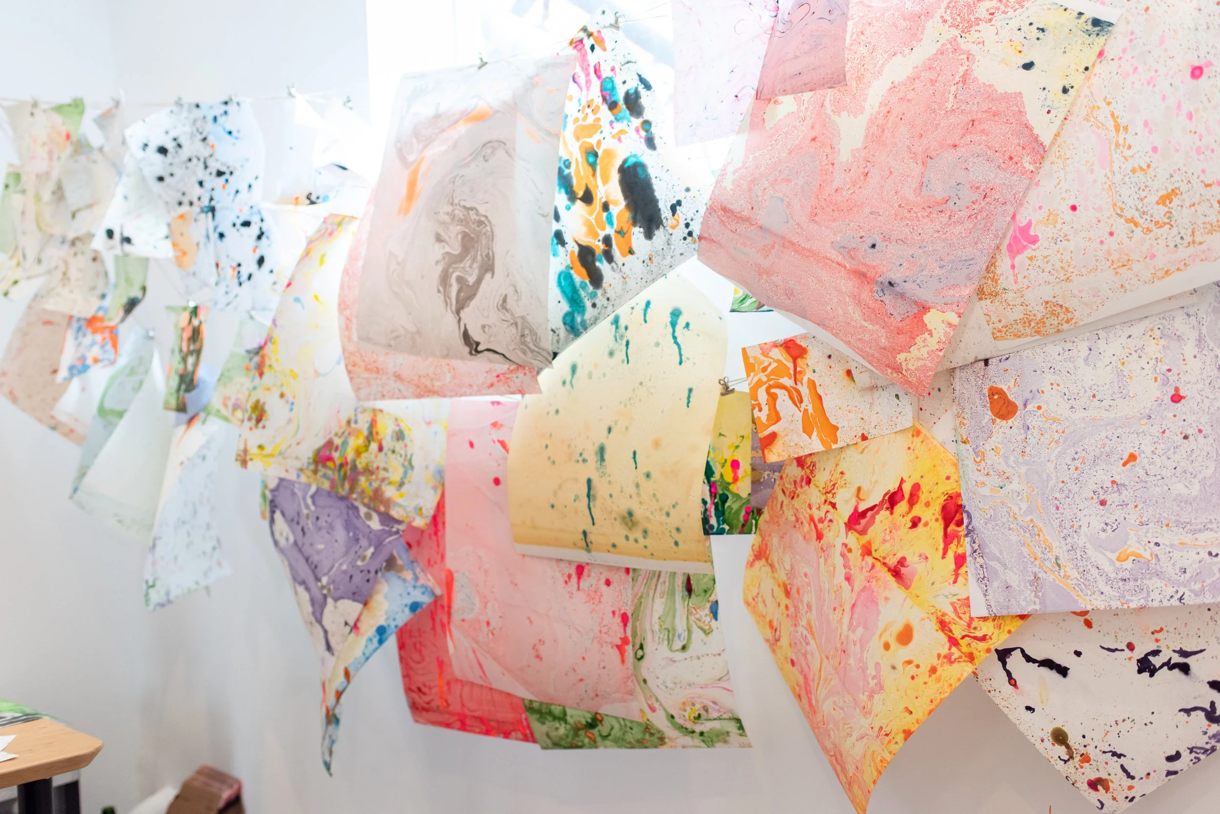 Colorful abstract paintings or drawings on crumpled, hanging paper sheets in an art studio or gallery.
