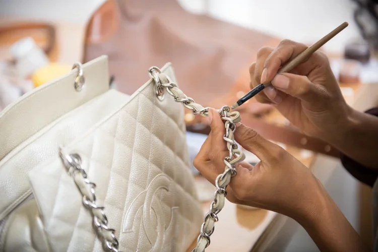 A person repairing or customizing a white quilted leather handbag with a silver chain strap.