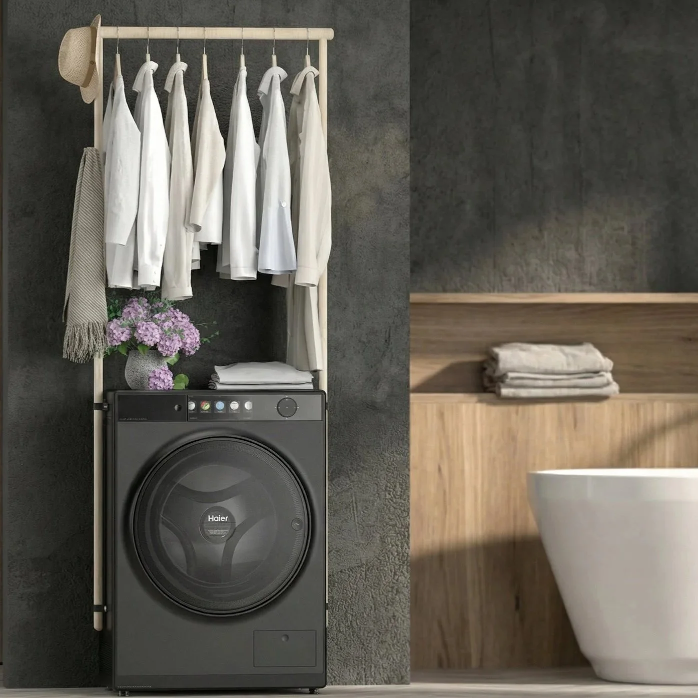 Laundry room with a black washing machine, a wooden shelf with folded towels, a vase of purple flowers, a hanging rack with white shirts and a hat, and a bathroom with a white toilet and wooden accents.