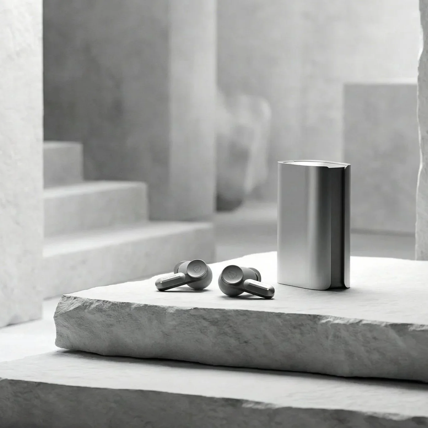 Silver wireless earbuds and a matching charging case on a textured stone surface in a minimalistic, monochrome setting.