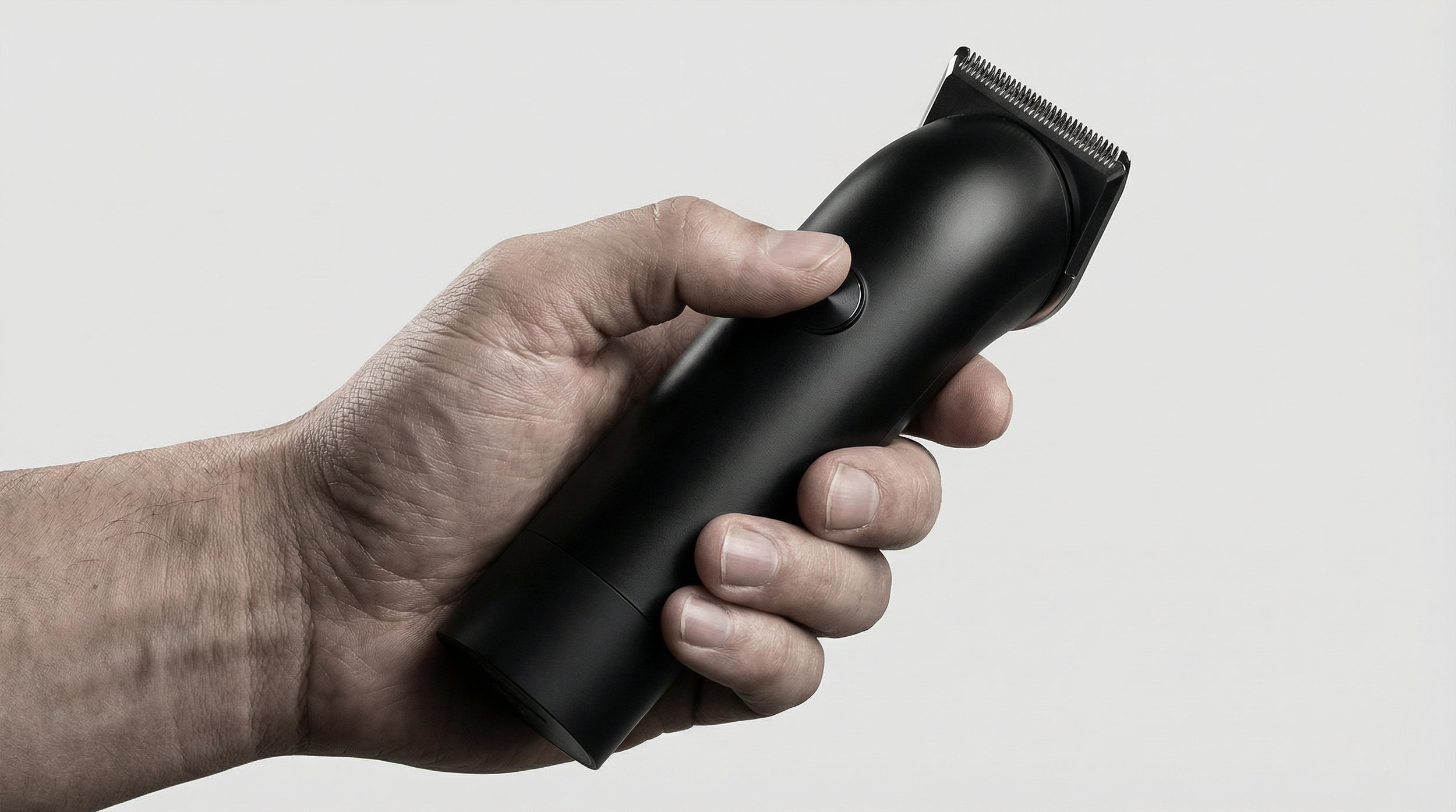 A hand holding an electric hair clipper with a black body and a silver blade against a plain white background.