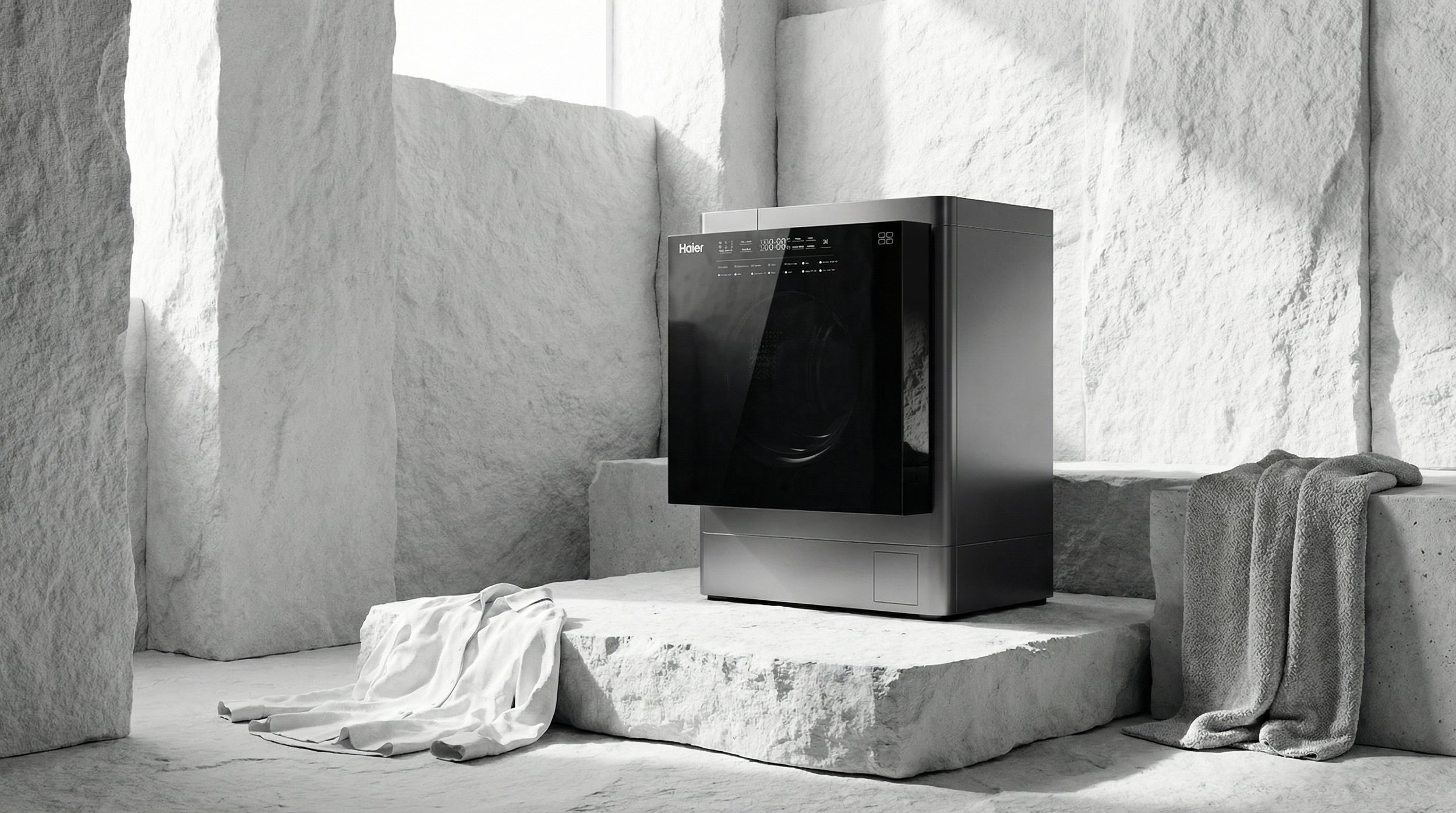 Black and silver washing machine in a minimalist white stone setting with towels draped over stones and on the floor.