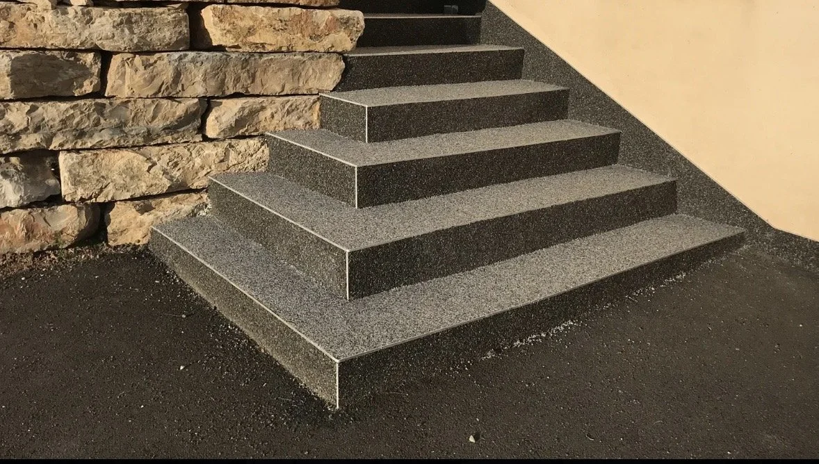 Escalier en pierre noire avec une paroi en pierre de roche à gauche et un mur beige à droite.