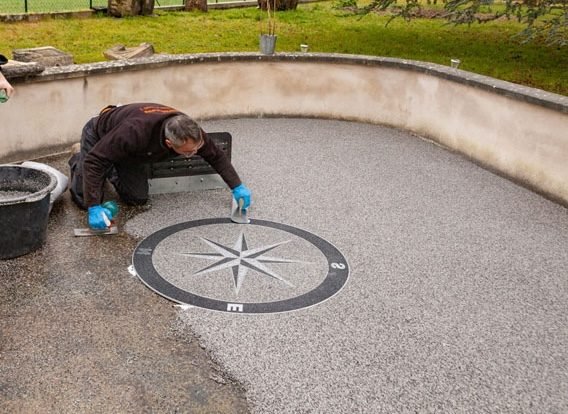 Une personne en train de travailler sur l'installation d'une boussole géante en pierre dans un espace extérieur.
