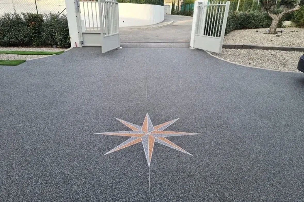 Une allée pavée avec un motif en étoile au centre, ouvrant sur une entrée de clôture blanche.