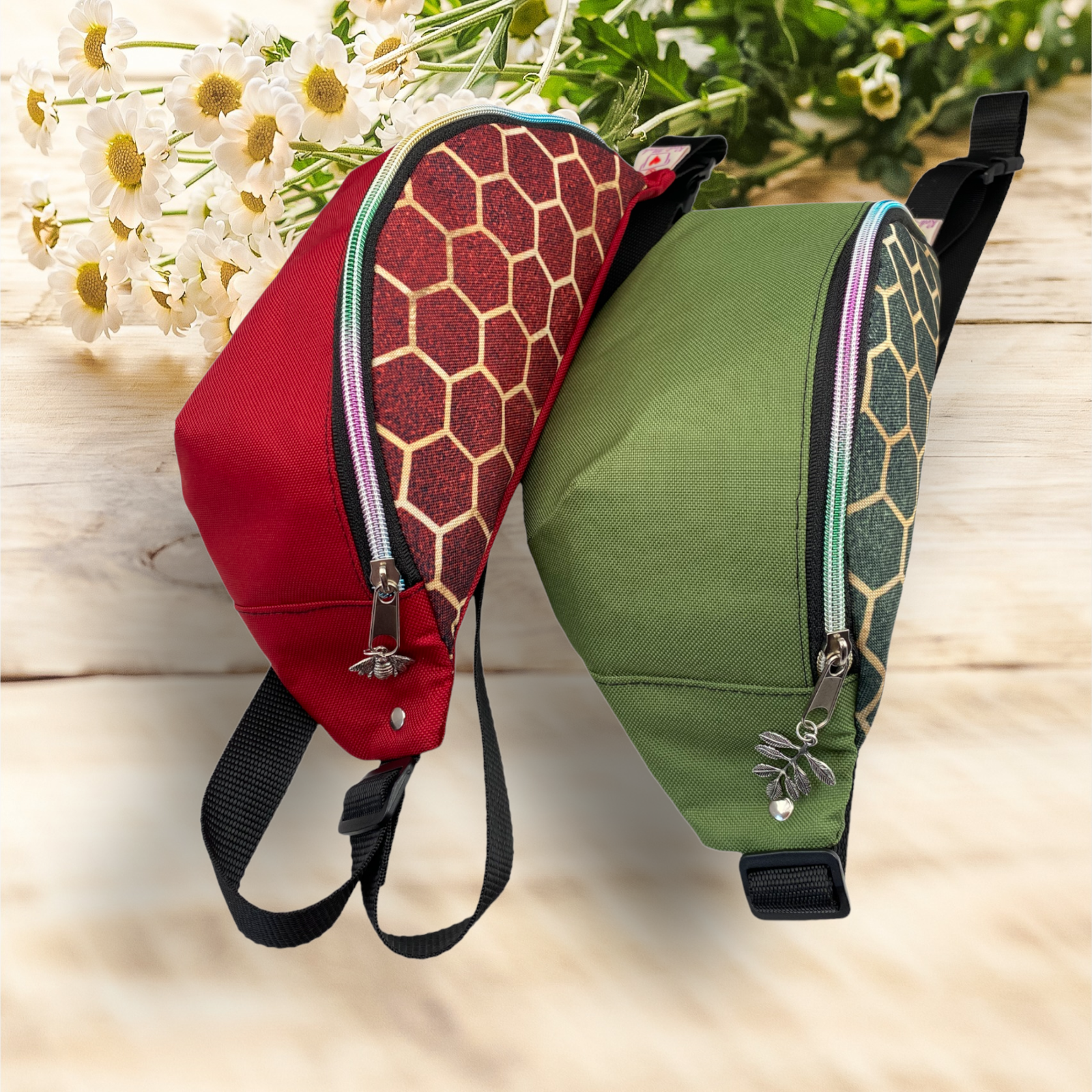Two colorful backpacks, one red with a honeycomb pattern and one green with a hexagon pattern, resting on a wooden surface with white flowers in the background.