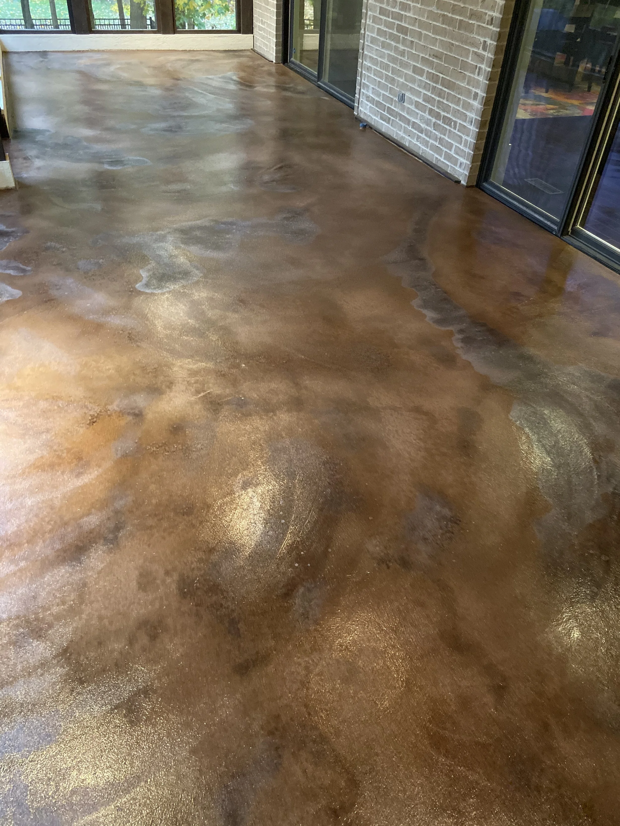 Polished concrete floor in a sunlit enclosed porch with brick wall and large glass doors.