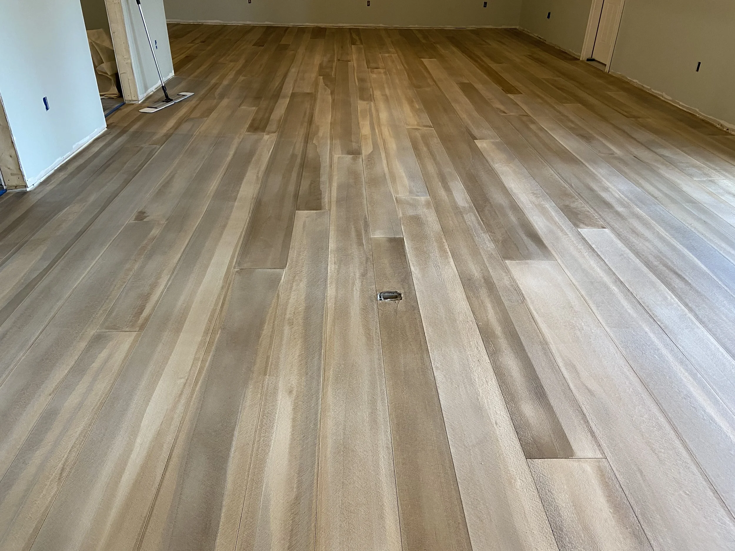 Newly installed light-colored hardwood flooring in a room under construction, with some tools and unfinished walls visible.