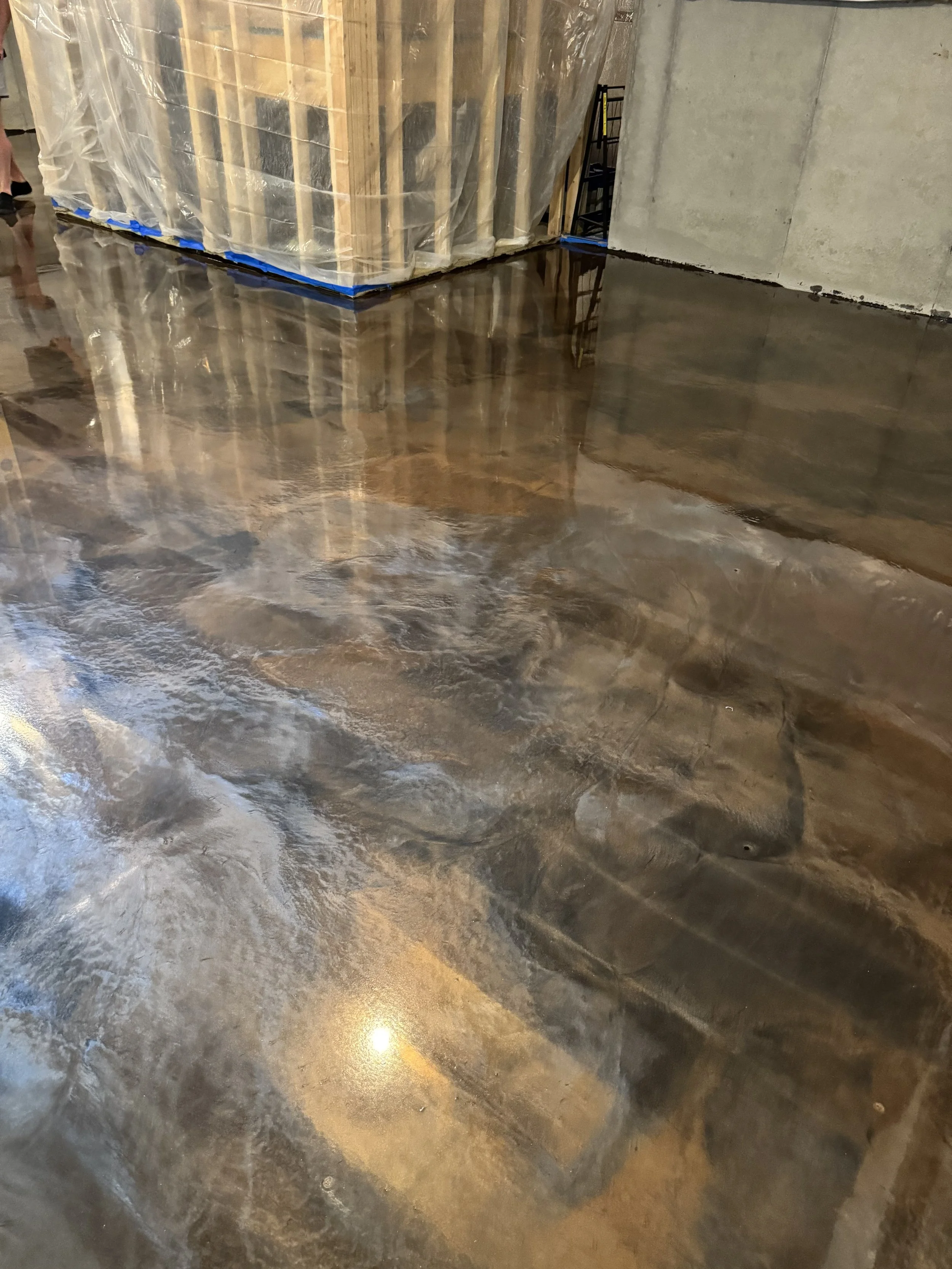 A polished concrete floor reflecting ceiling lights in an unfinished room with exposed wood framing and a plastic-covered structure.