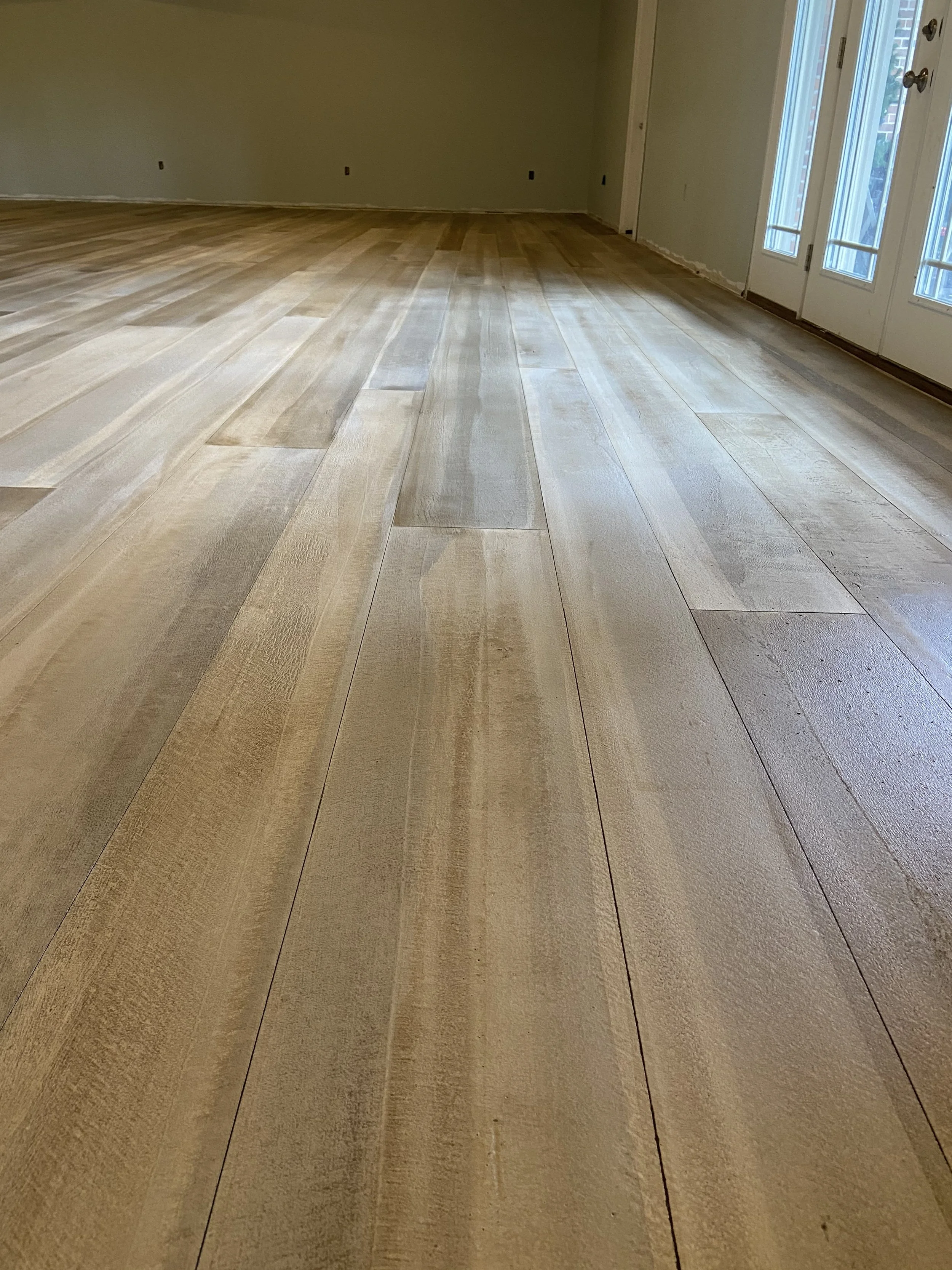 Room with new light-colored wooden flooring and sliding glass door leading outside.