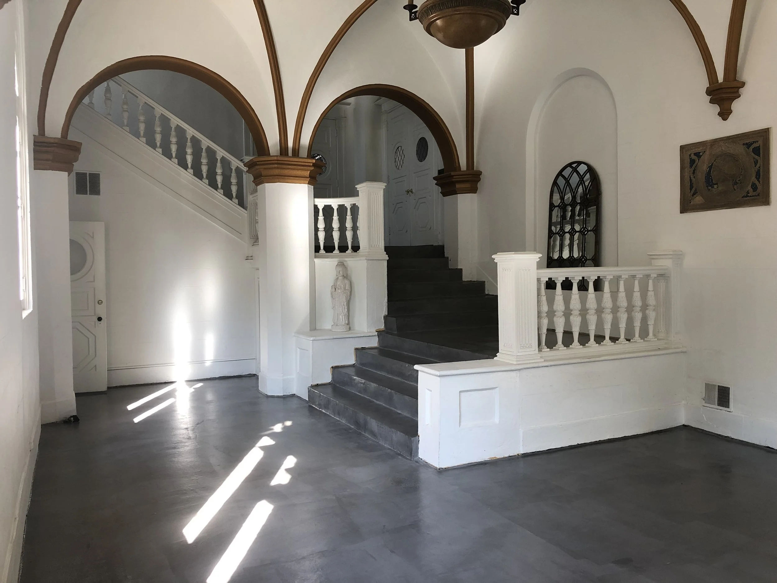 Interior view of a staircase with dark steps, white balustrades, and arched ceiling details with wood accents.