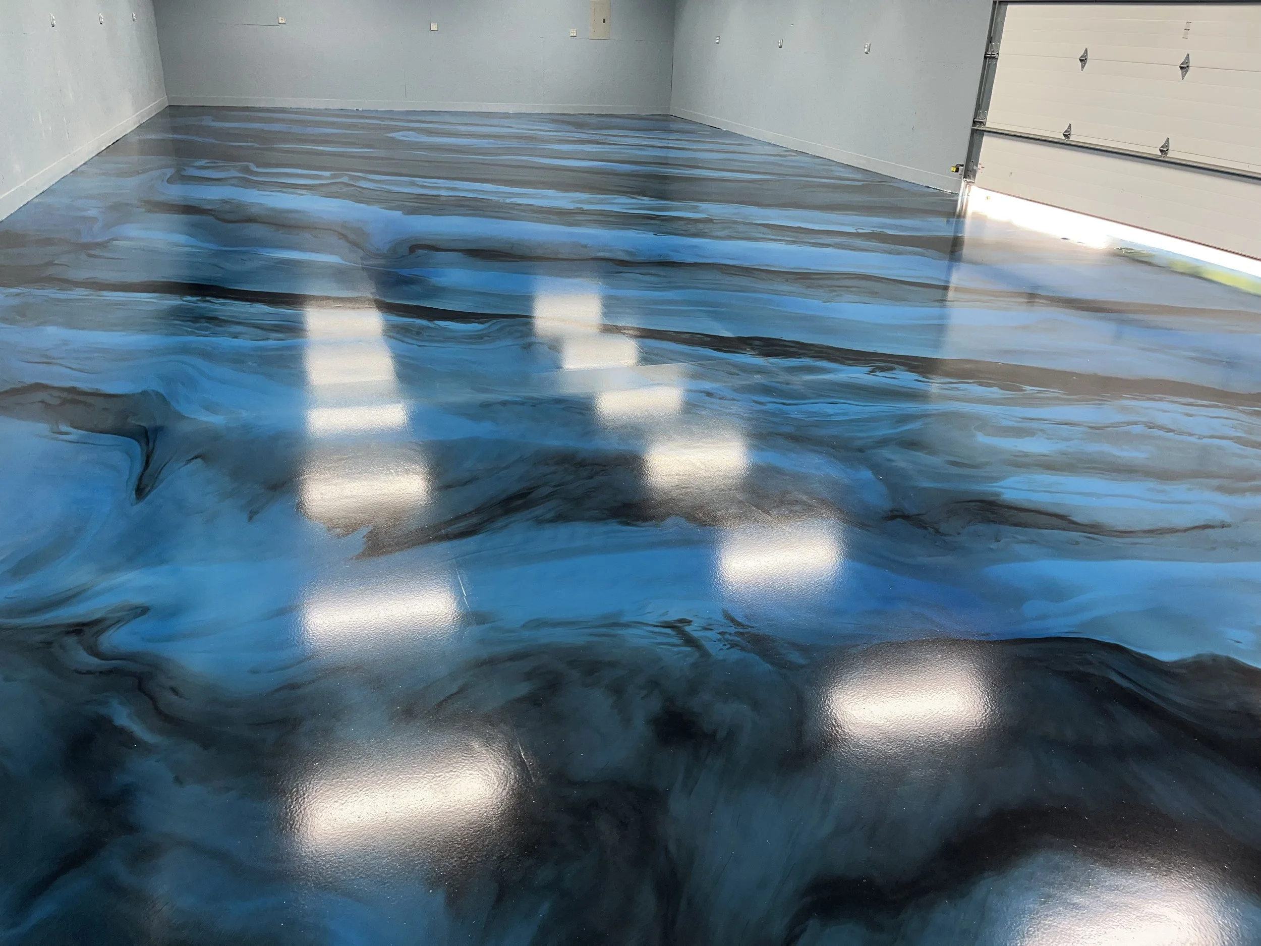 Interior of a garage with a custom epoxy floor featuring swirling blue, black, and white patterns that resemble water or marble.