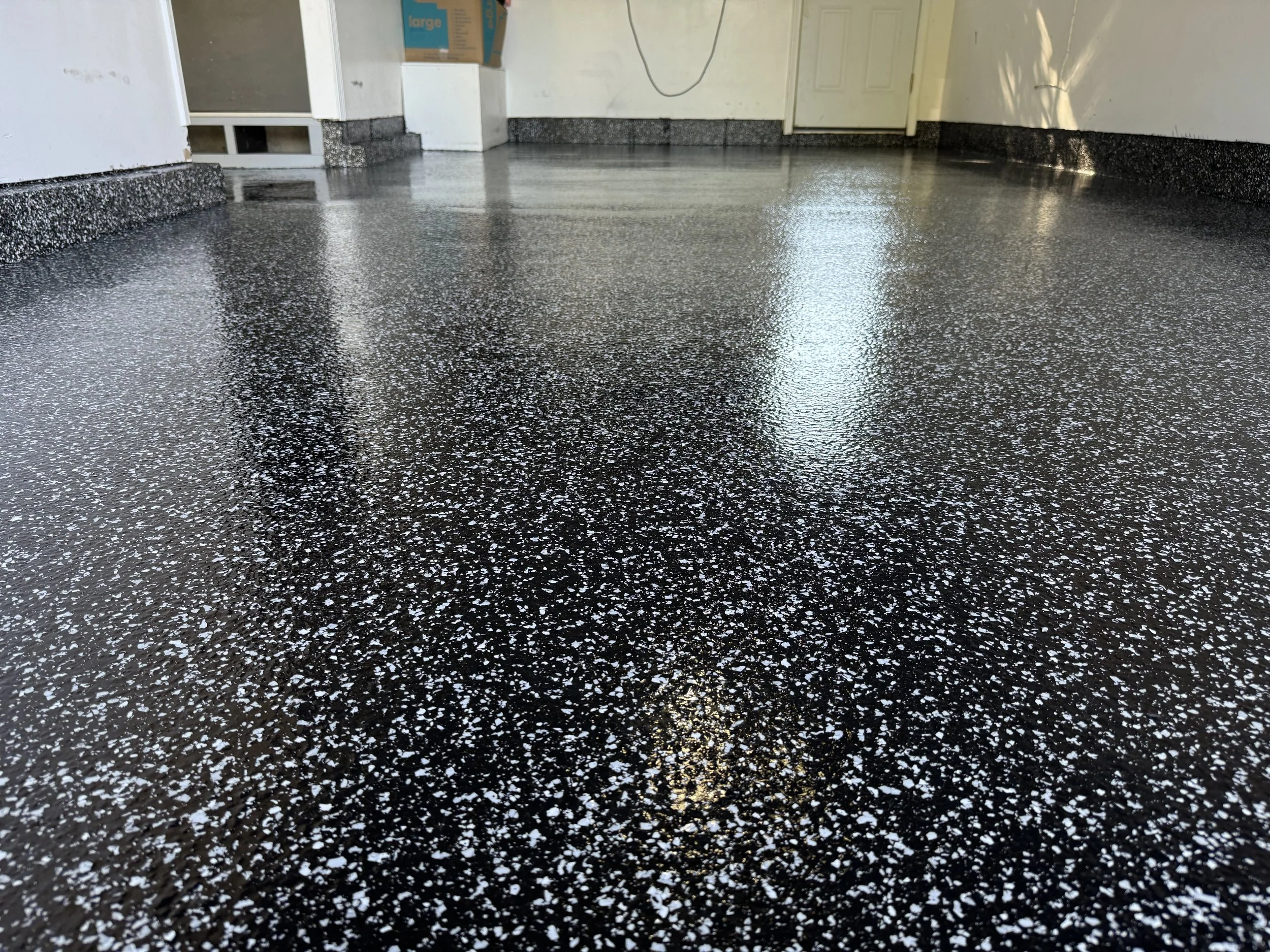 Polished black epoxy floor with white specks in a garage or interior space.
