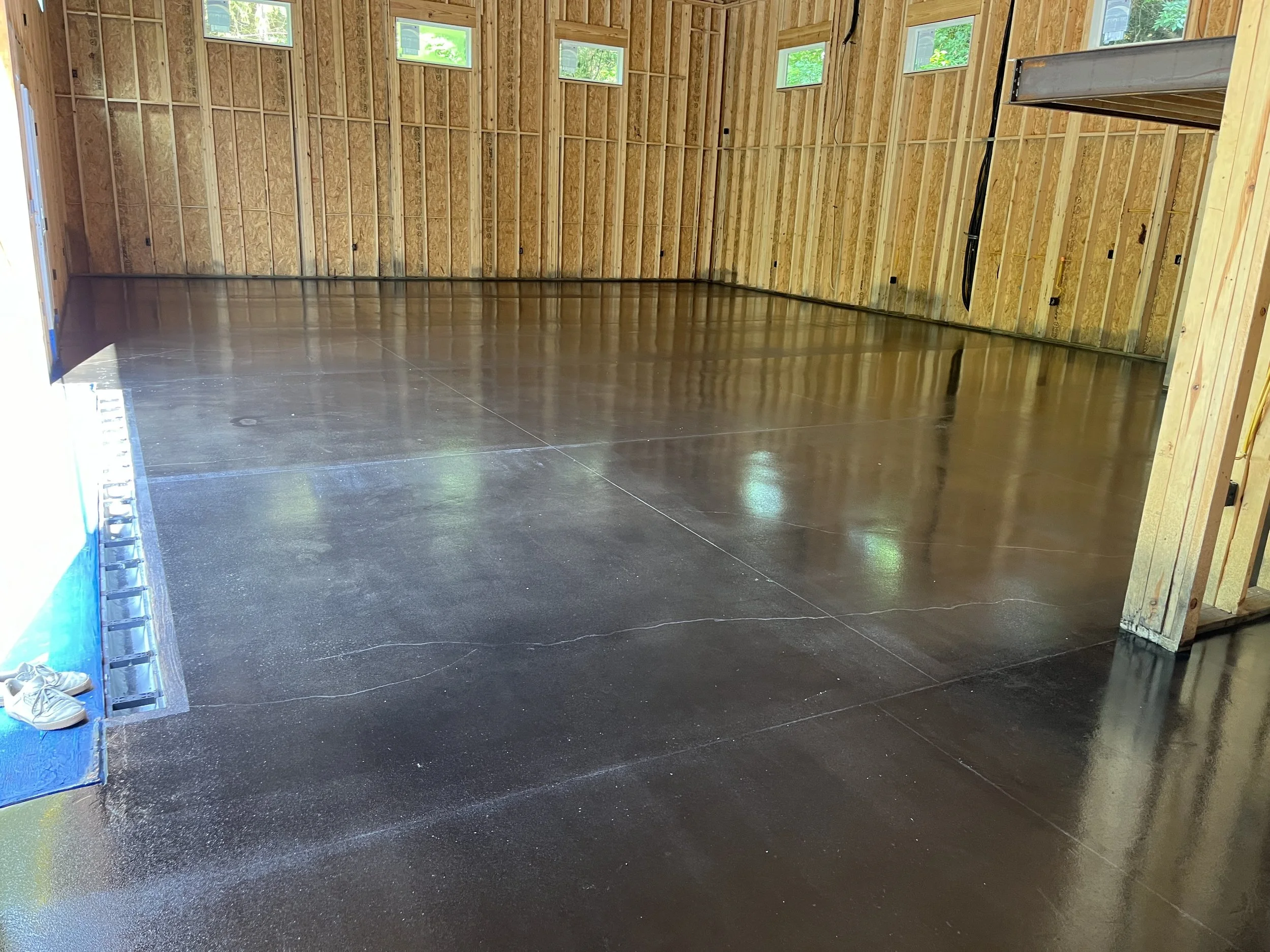 Empty garage with a polished concrete floor, unfinished wooden walls, and small windows near the ceiling allowing natural light.
