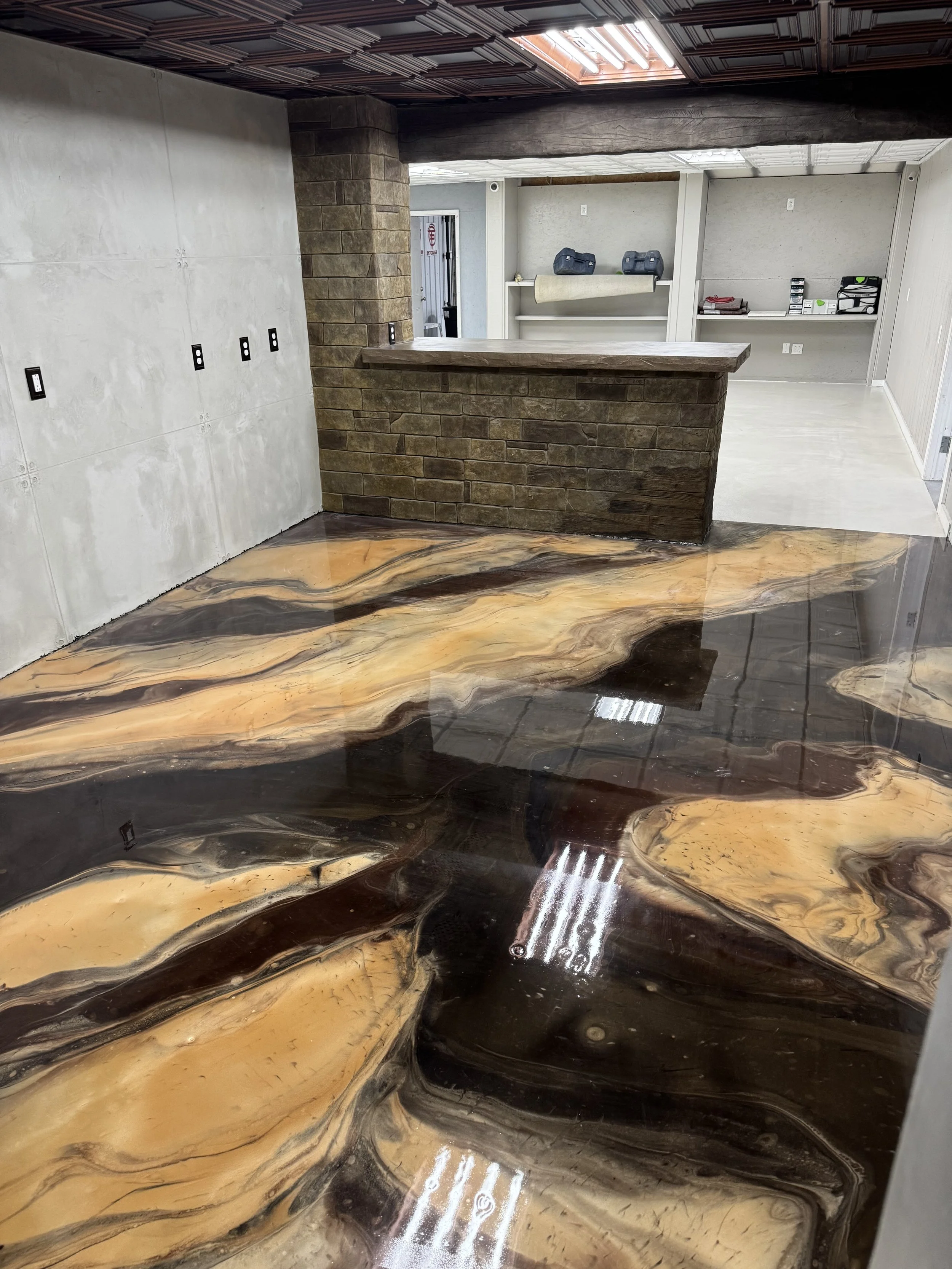 A room with a highly polished, multicolored marble floor, a brick bar with a wooden top, and a wall with shelves containing tools and supplies.