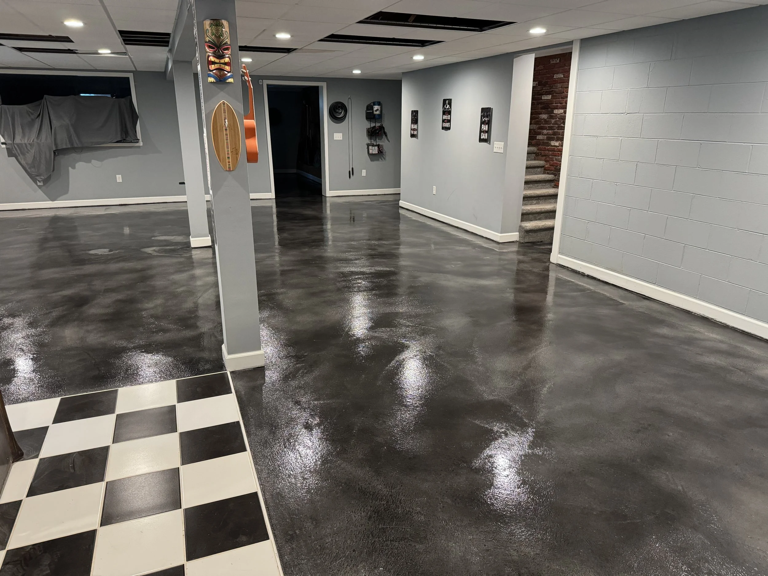 Empty basement room with polished concrete floors, a staircase with carpet steps, and a partial view of a checkerboard floor pattern at the entrance.