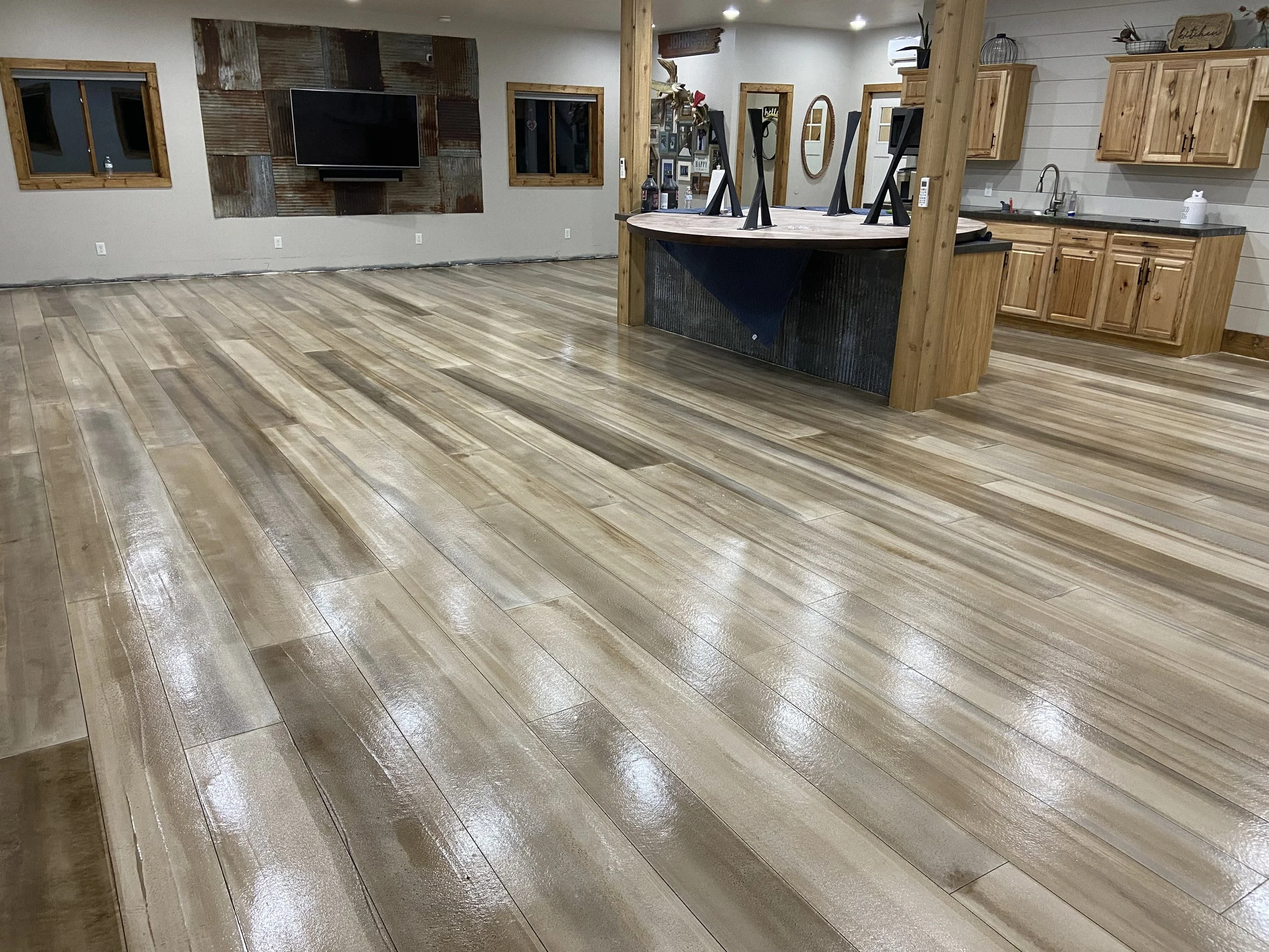 Empty room with polished wooden floor, a wall-mounted TV, and a kitchen area with wooden cabinets and a large countertop island.