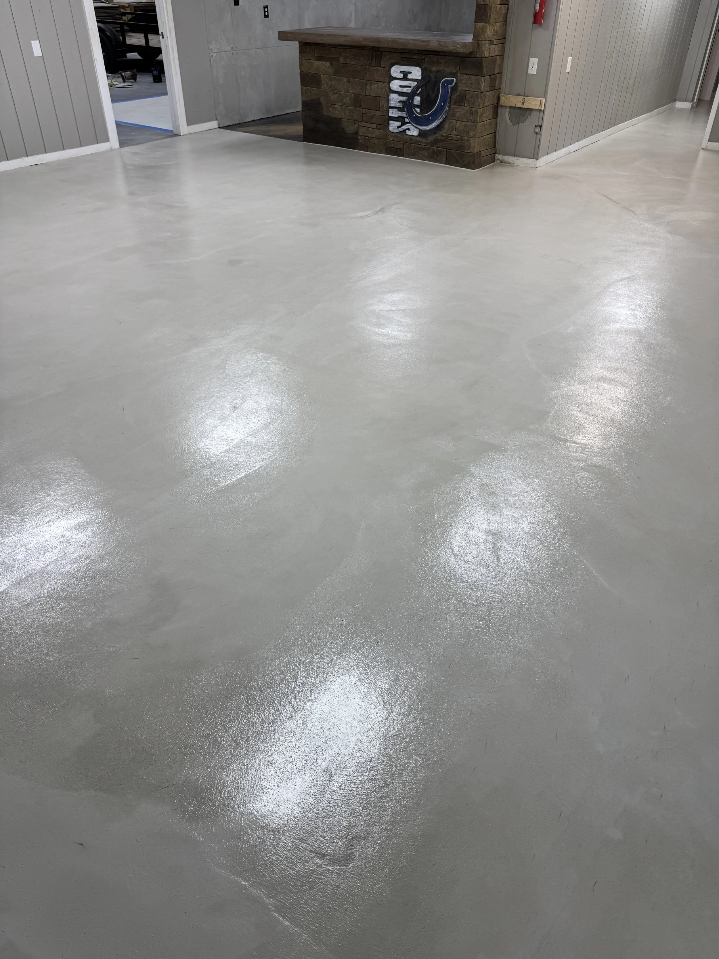 Polished concrete floor in an indoor space with gray walls, a brick corner with a Colts sign, and a doorway leading to another room.