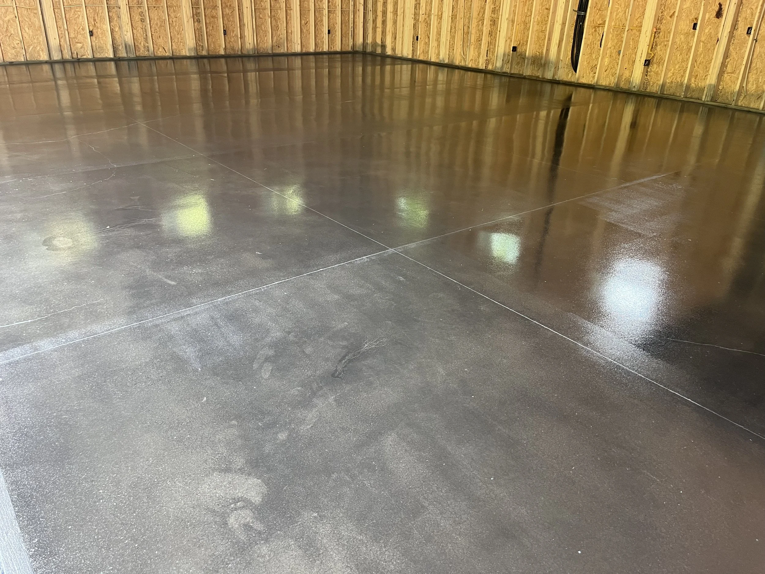 Freshly poured and sealed concrete floor in a garage or workshop with unfinished wooden walls.