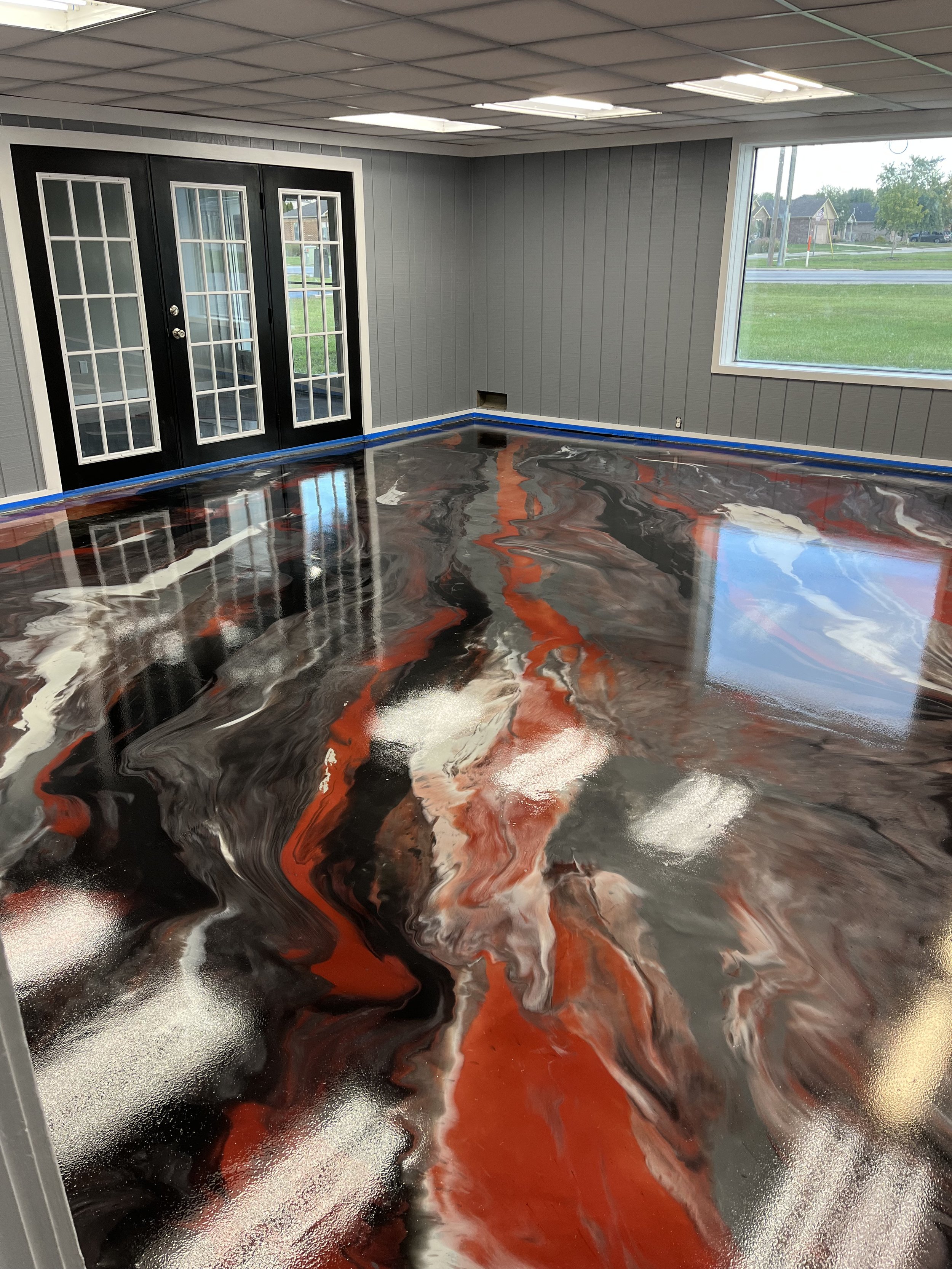 Room with gray walls, black double doors with glass panes, large window, and a floor with a swirling, marbled design in black, white, gray, and orange.