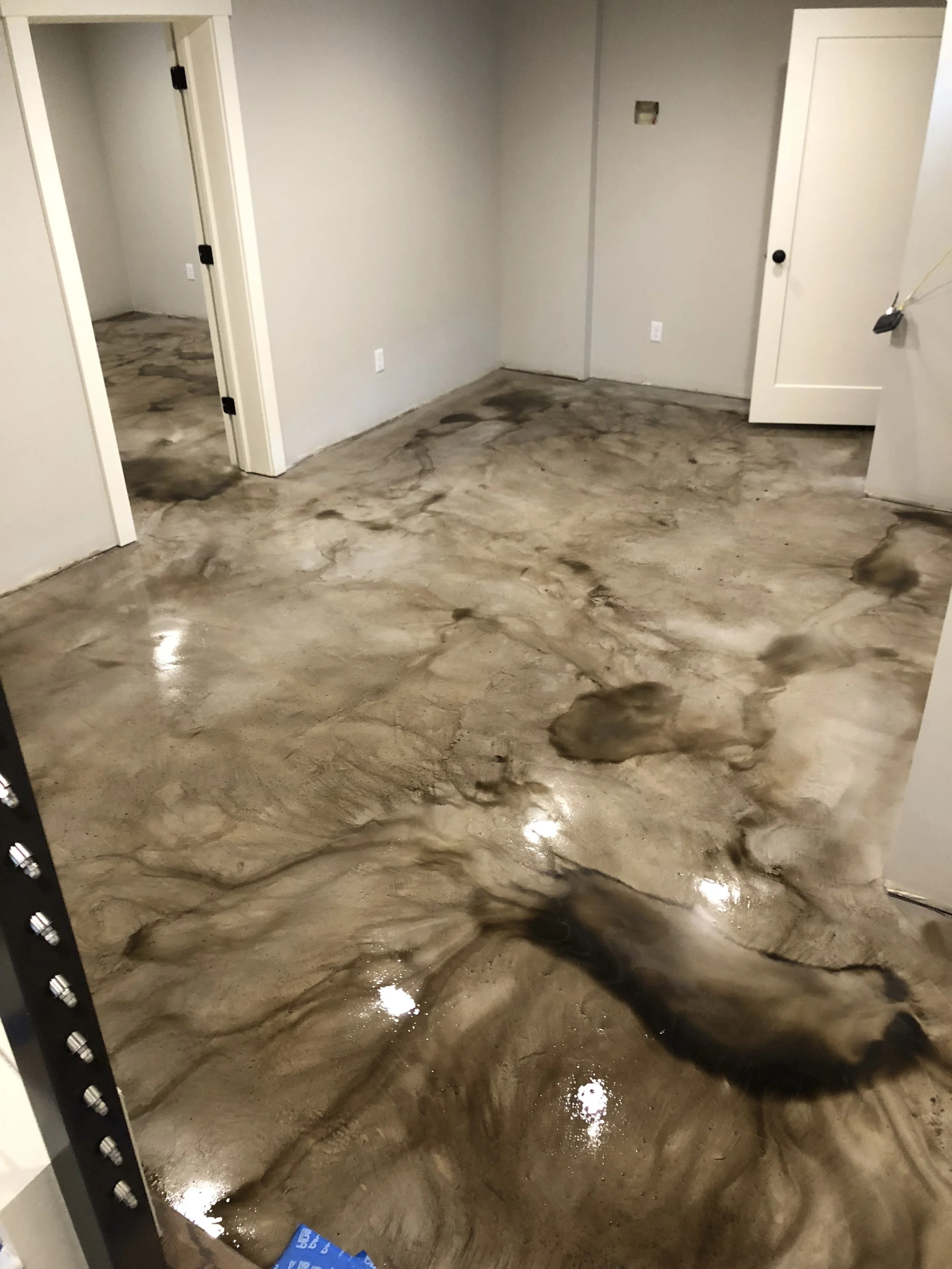 Room with polished concrete floor that has dark stains and marble-like veining, with plain light-colored walls and white doors.