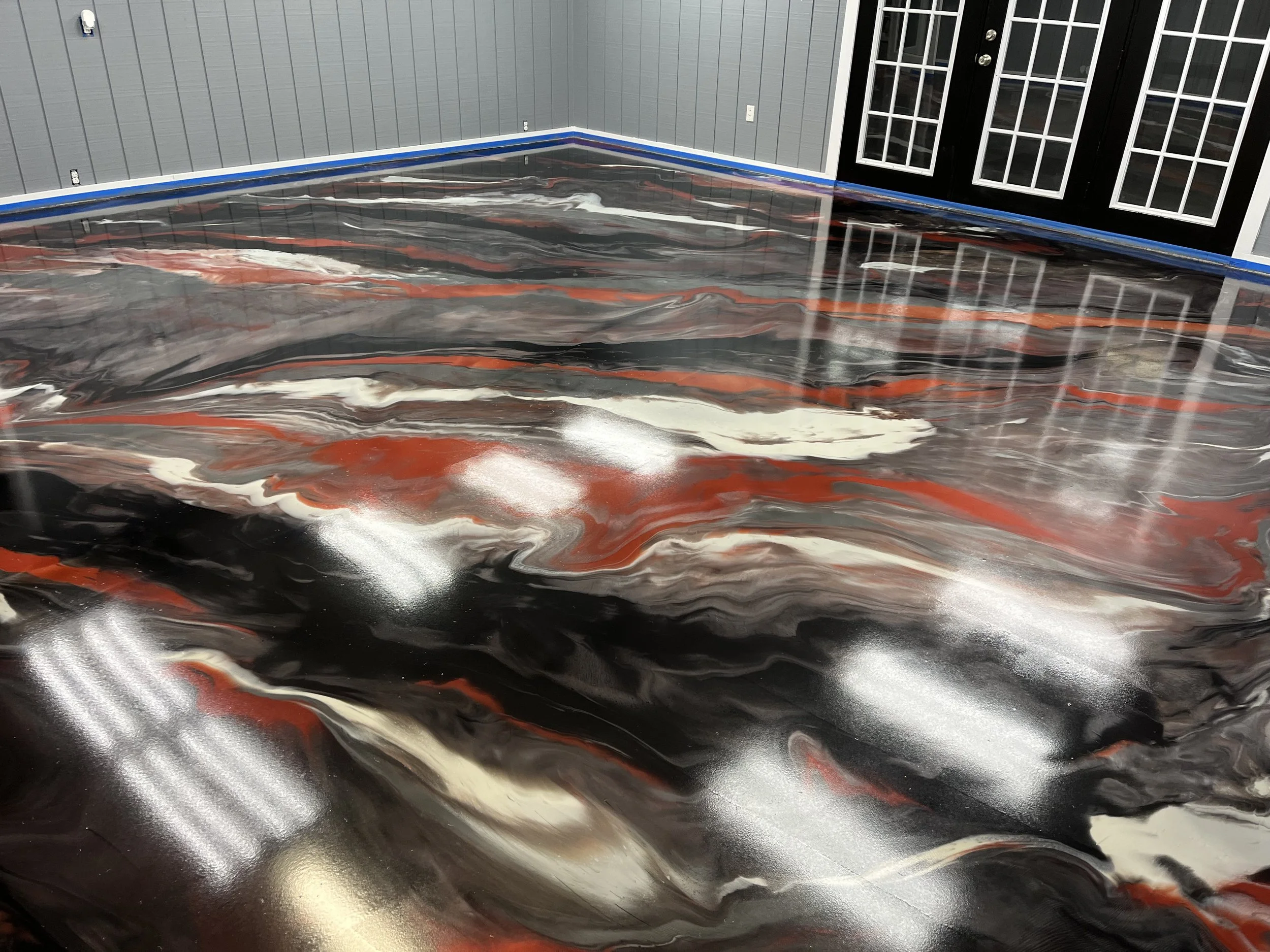 A room with a painted floor that features swirling black, white, red, and gray patterns. The room has gray walls, a blue border along the baseboards, and black double doors with multiple glass panes.