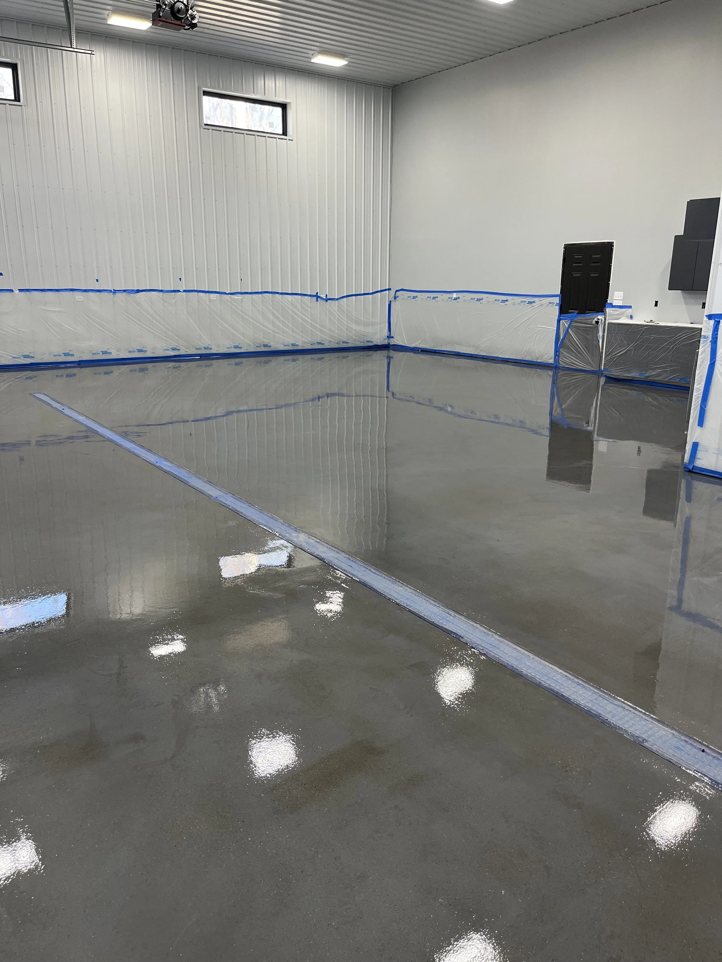 Clean and polished concrete floor in an industrial or garage space with protective plastic barriers along the walls and small high windows on the upper part of the wall.