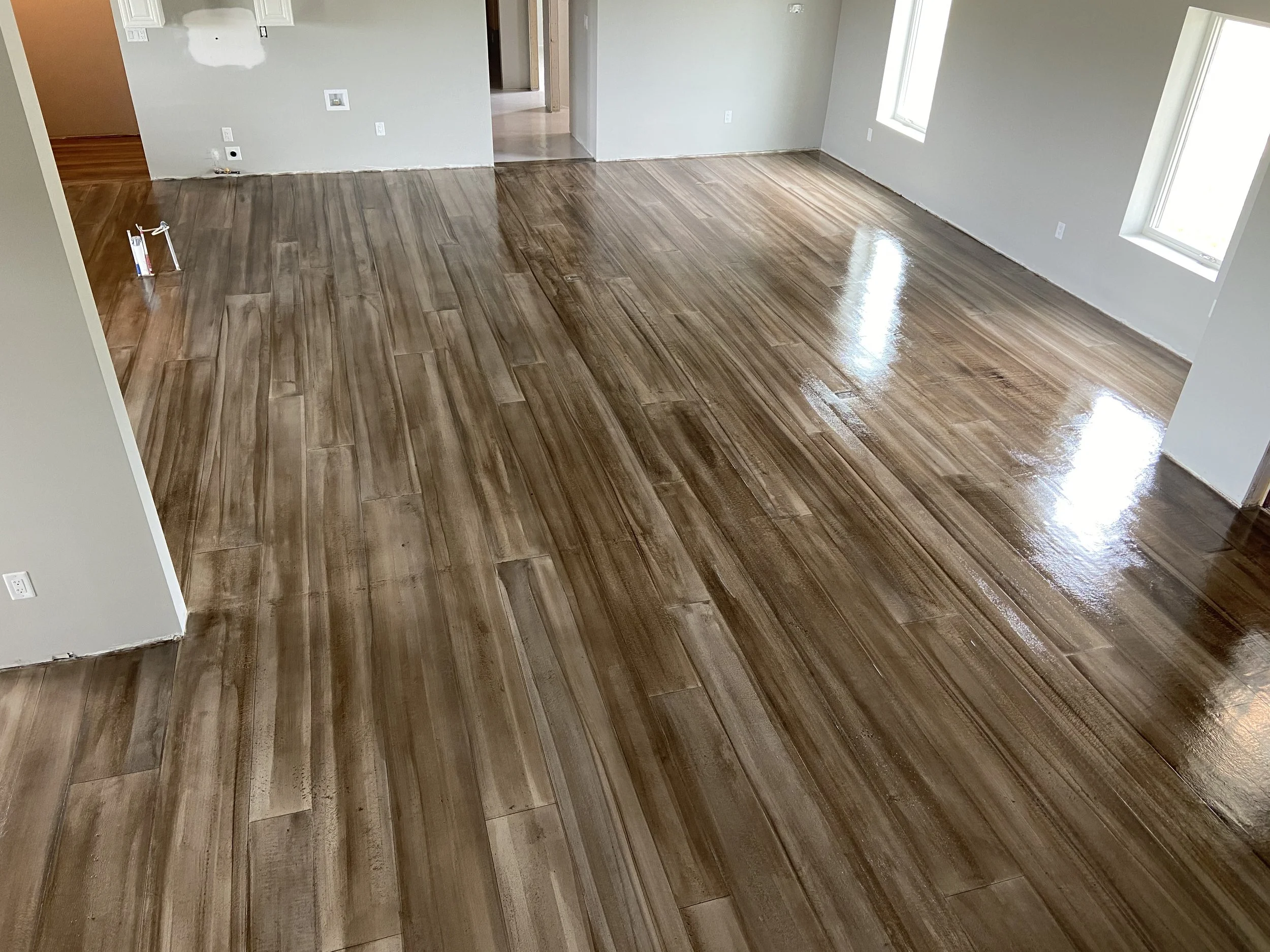 Empty room with newly installed glossy wood flooring and gray walls, with sunlight coming through two large windows.