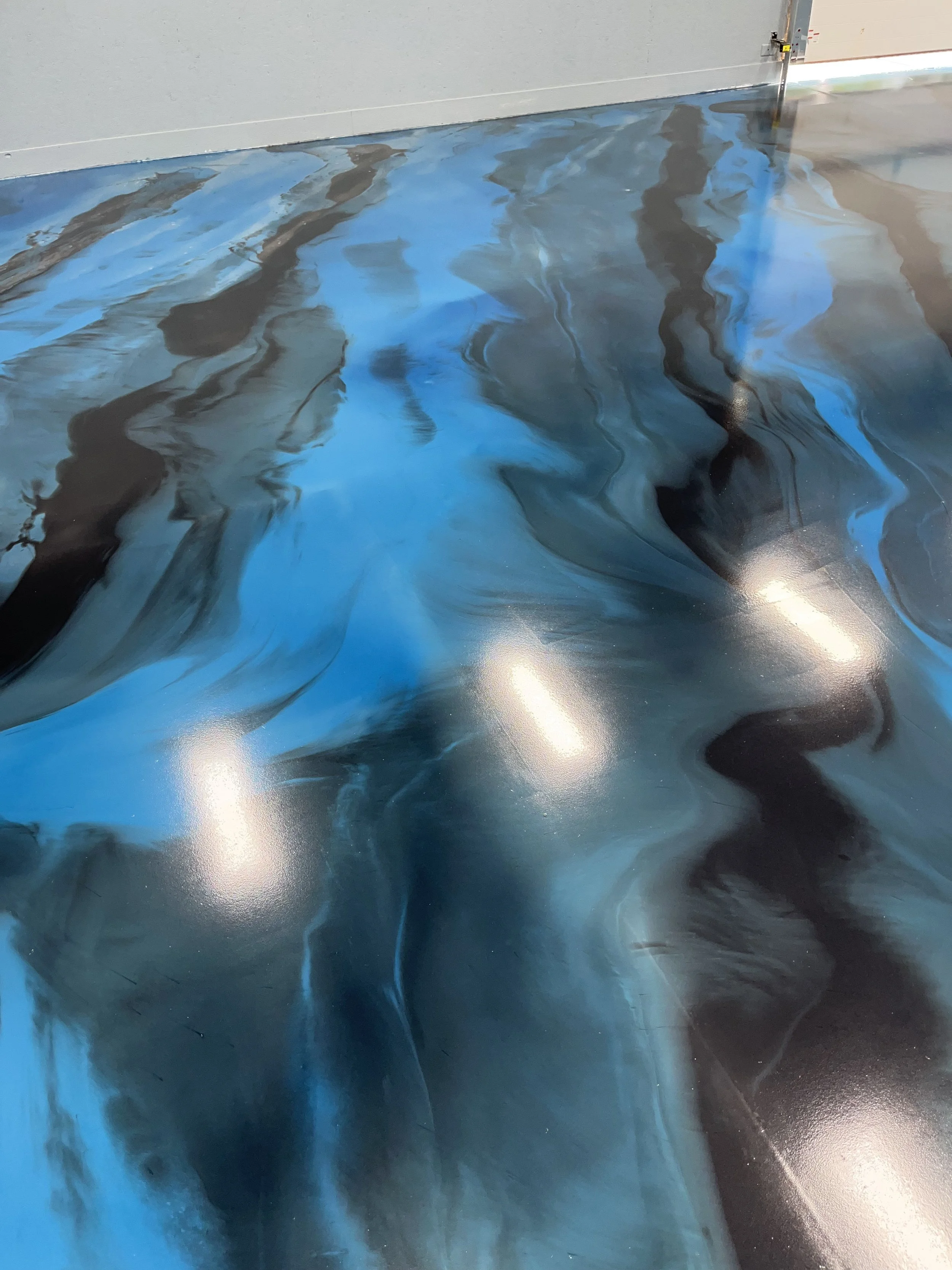 Close-up of a vibrant epoxy floor with swirling blue and black marbled pattern in a garage or industrial space.
