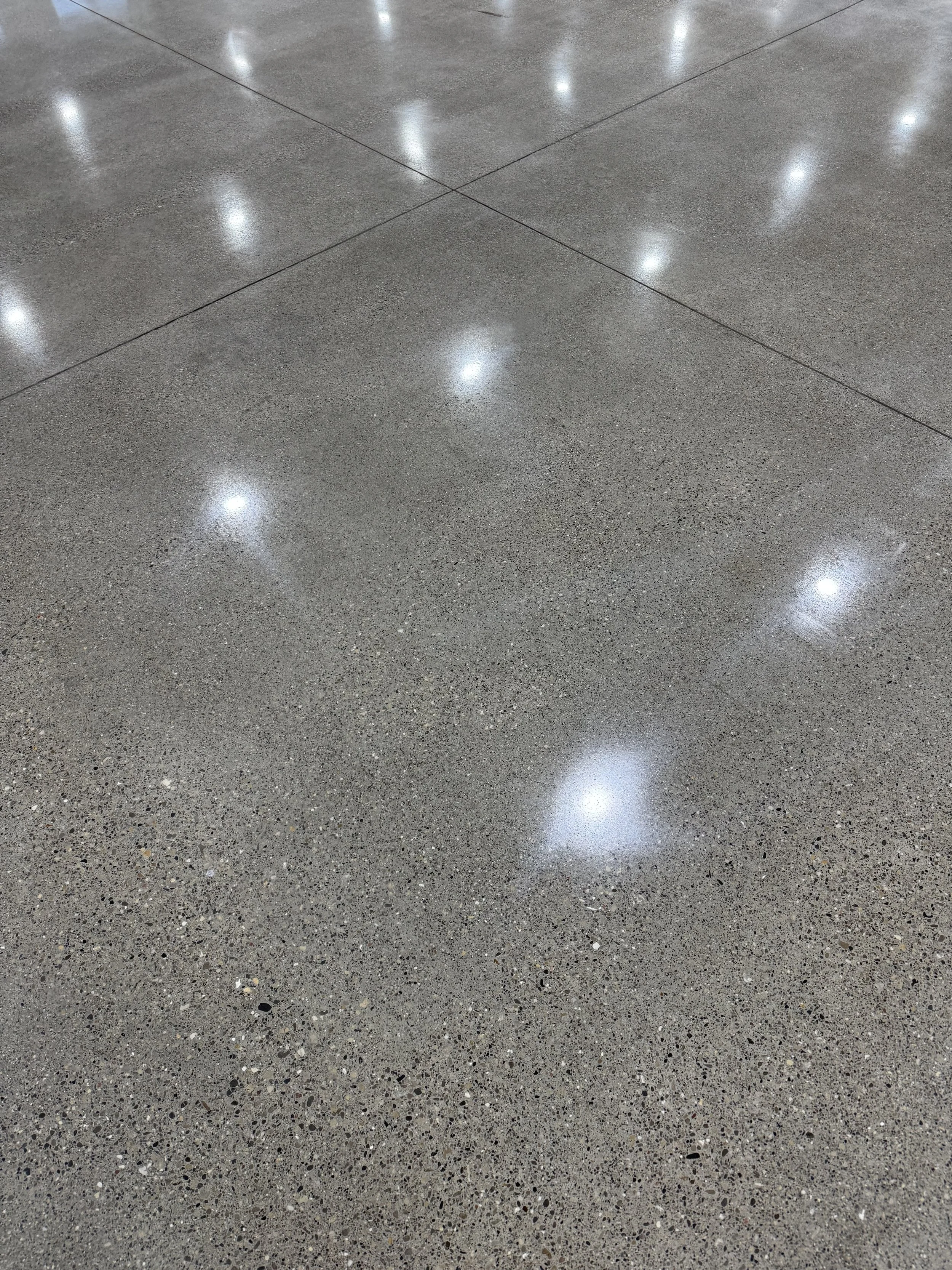 Shiny polished concrete floor with reflections of overhead lights.