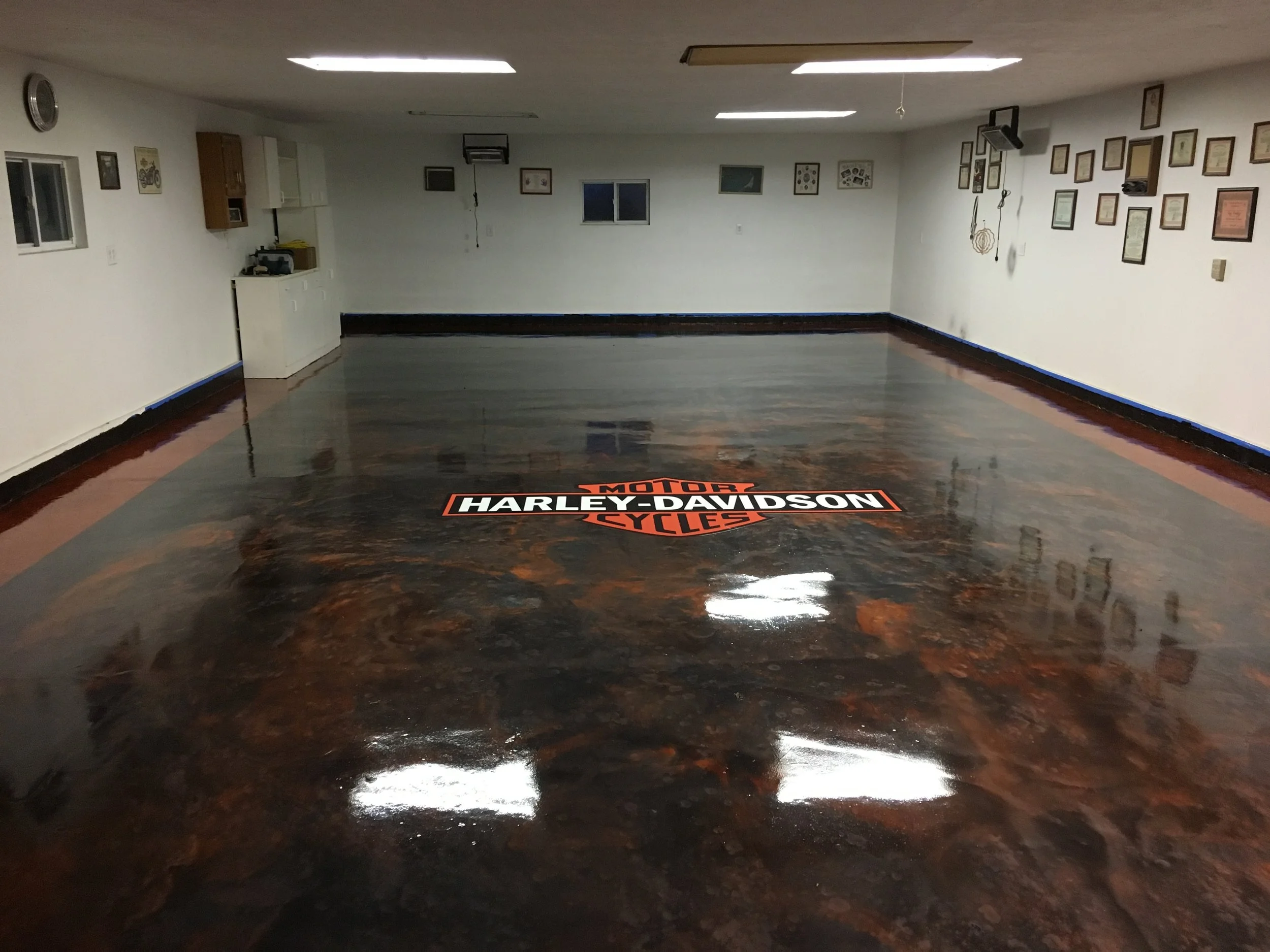 Empty room with white walls, framed pictures, and a Harley-Davidson logo on the shiny, polished concrete floor.
