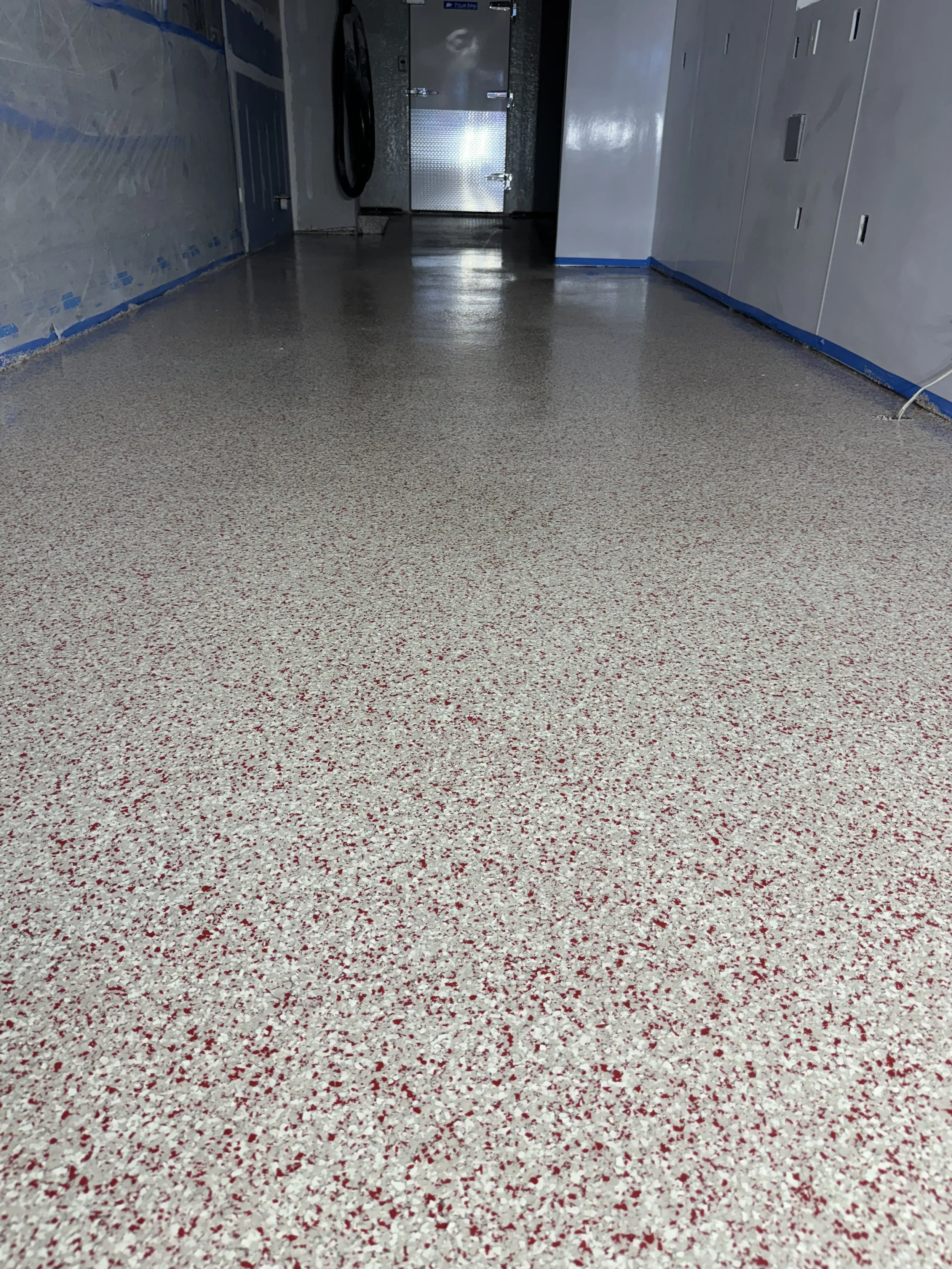Clean, speckled beige and red epoxy floor in a hallway, with metallic appliances and white walls.
