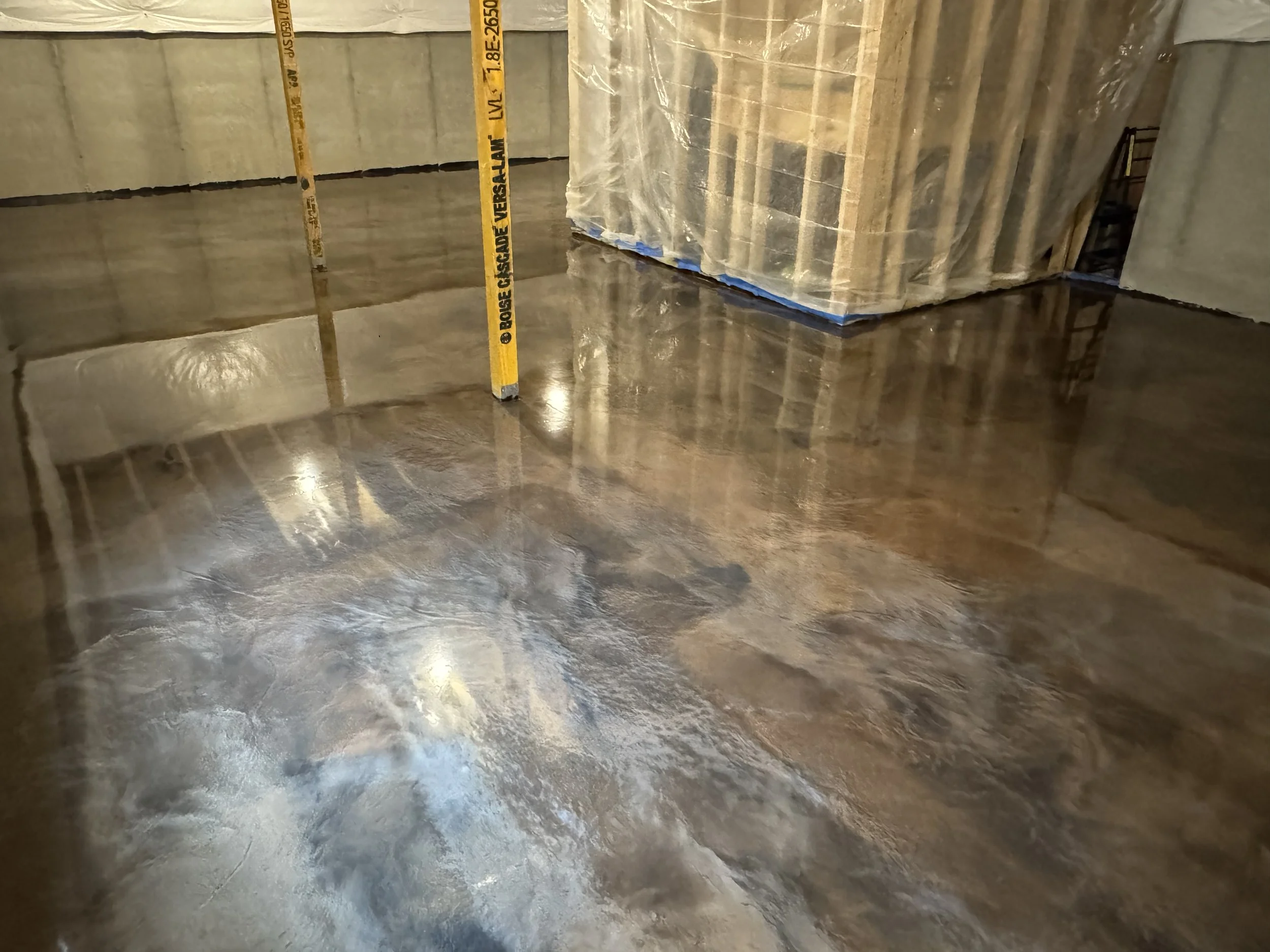 Polished concrete floor in a construction site with a yellow construction pole and wrapped pallets in the background.