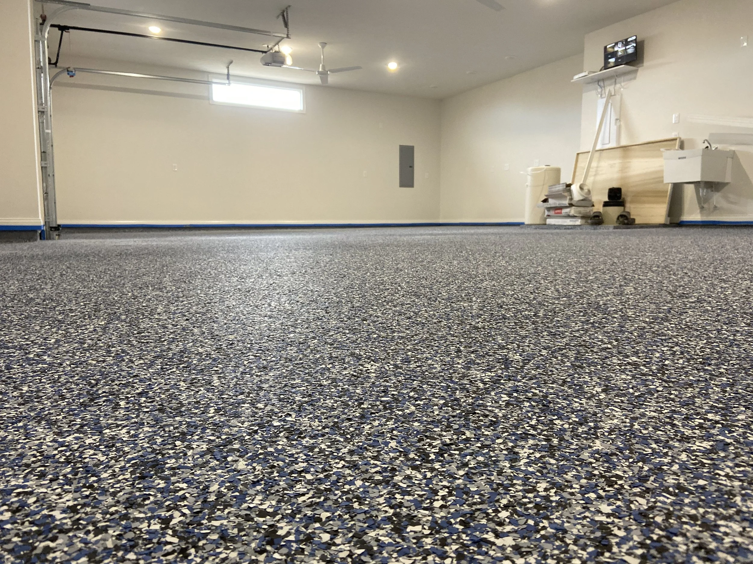 Empty garage with speckled gray and black carpet, white walls, and a small window