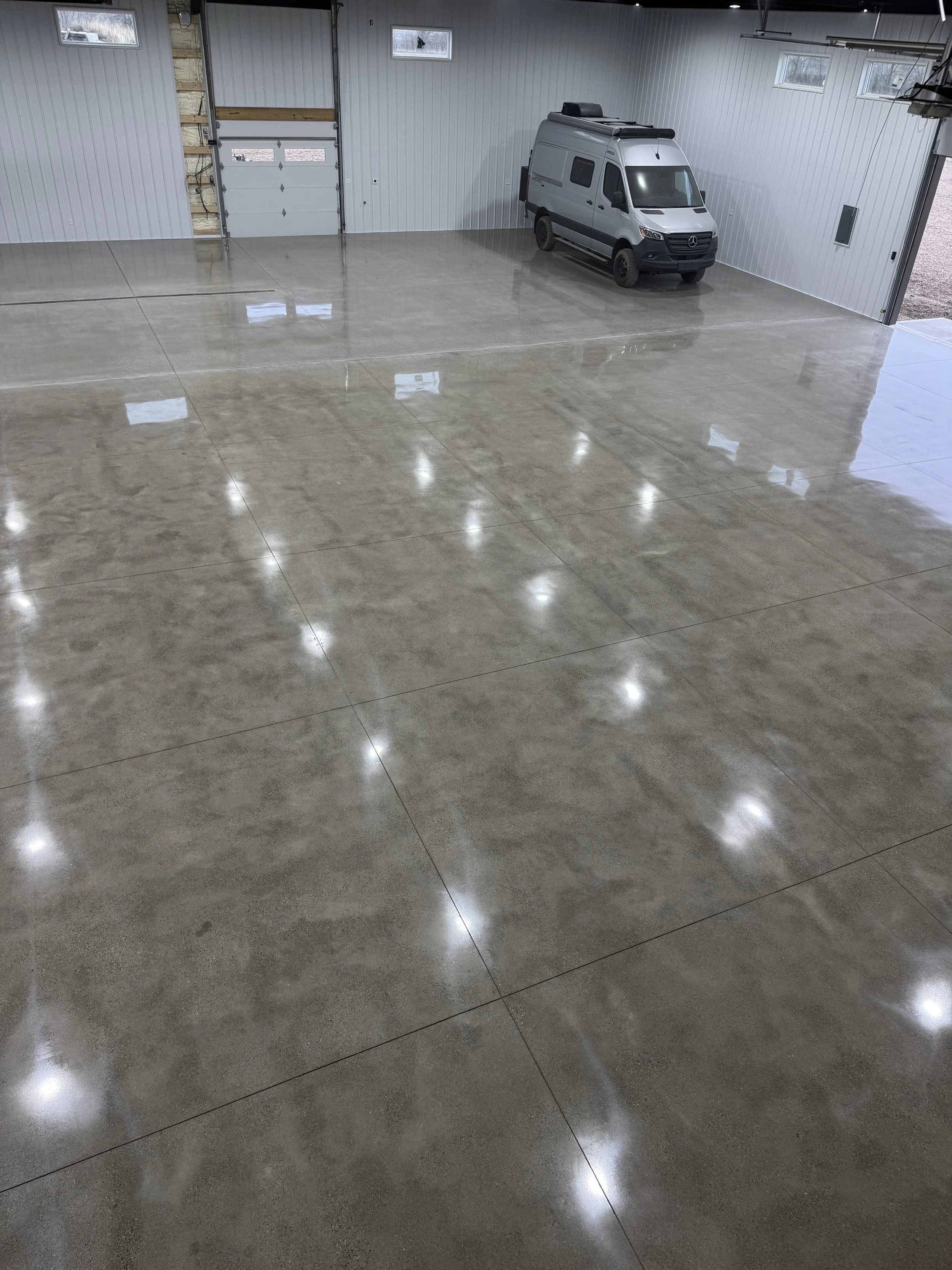 Empty garage with polished concrete floor, white walls, and a silver van parked inside near the back wall.
