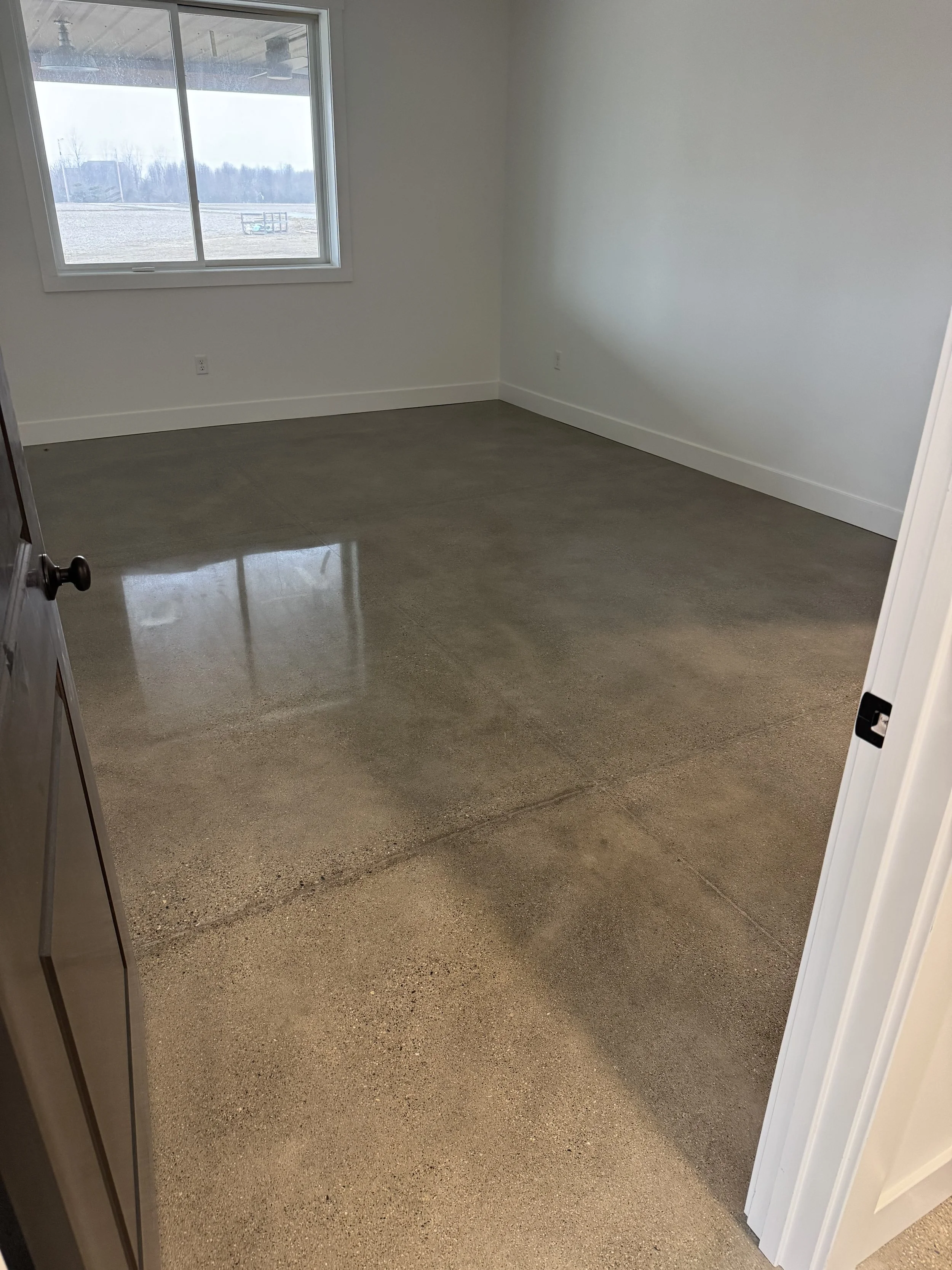 Empty room with polished concrete floor, white walls, and a window showing outdoor landscape with trees and sky.