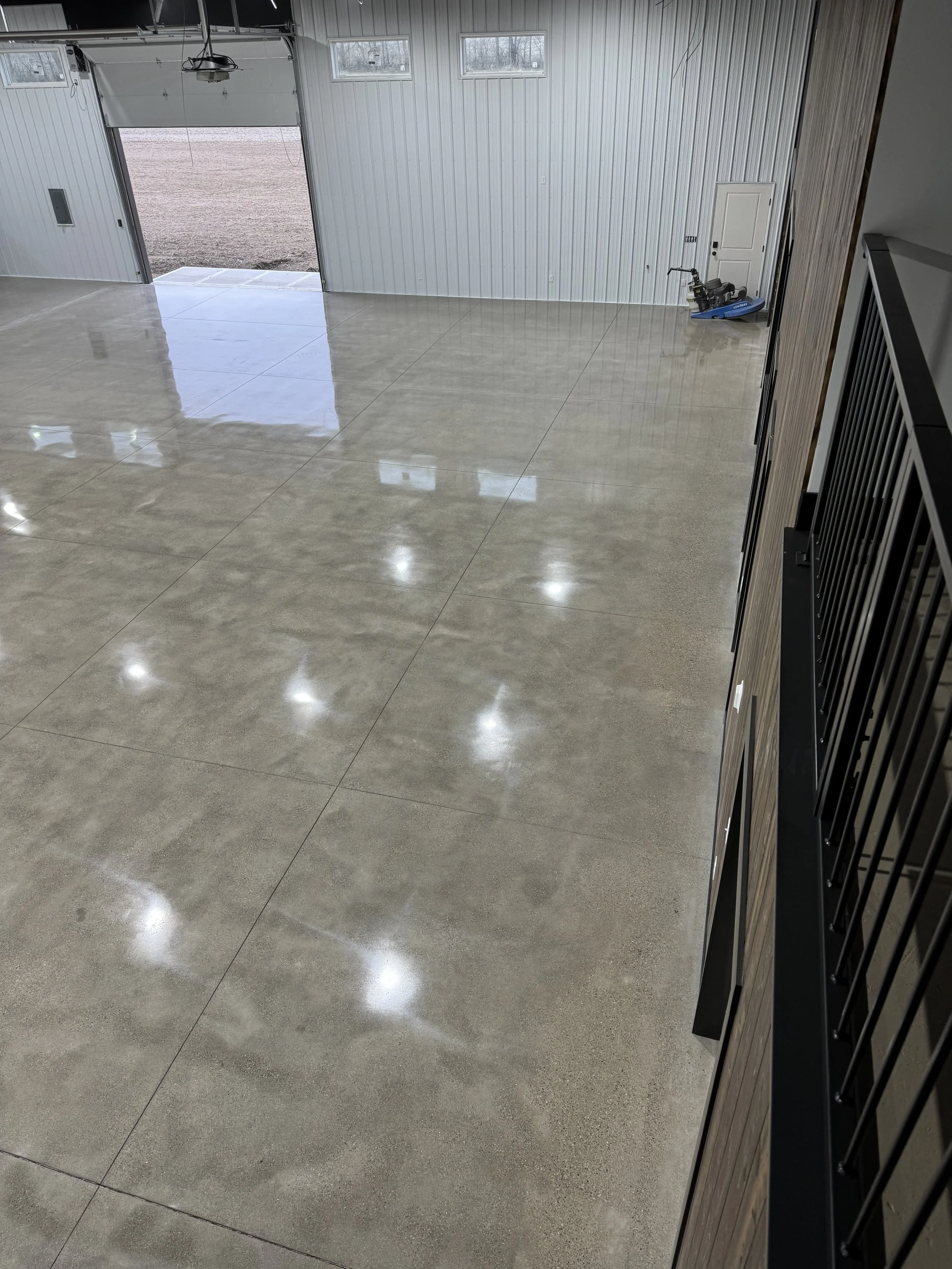 Empty industrial or garage space with a polished concrete floor, metal garage door open to outside, and a small snowmobile in the corner.